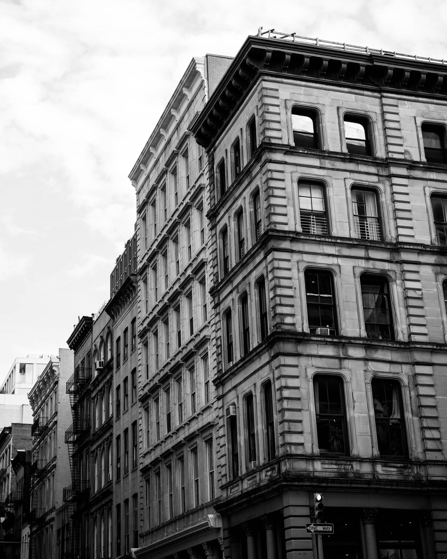 Black and white photo of historic multi-story brick and stone buildings with tall arched windows and fire escapes in a city district.