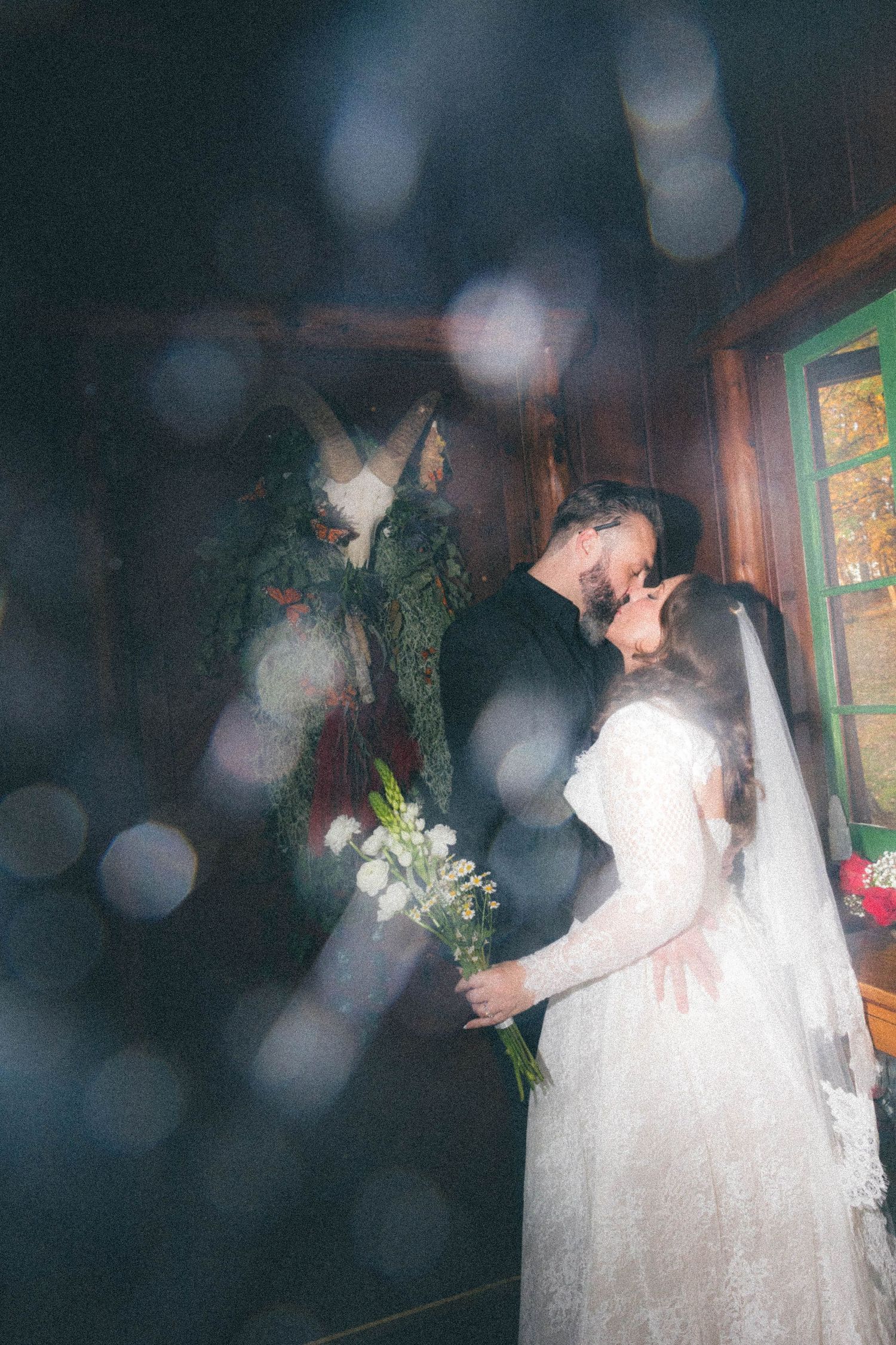 Bride and groom sharing a kiss in a rustic wooden venue with bokeh light effects.