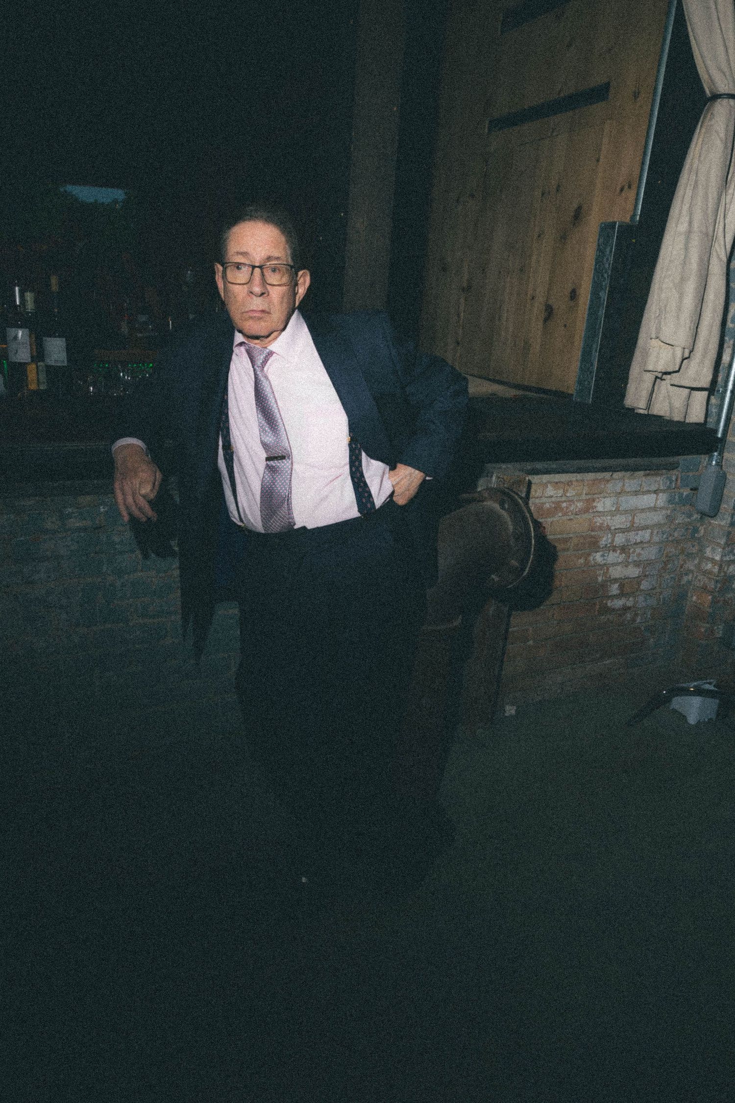 Older man in navy suit and lavender tie poses confidently at a dimly lit wedding venue.