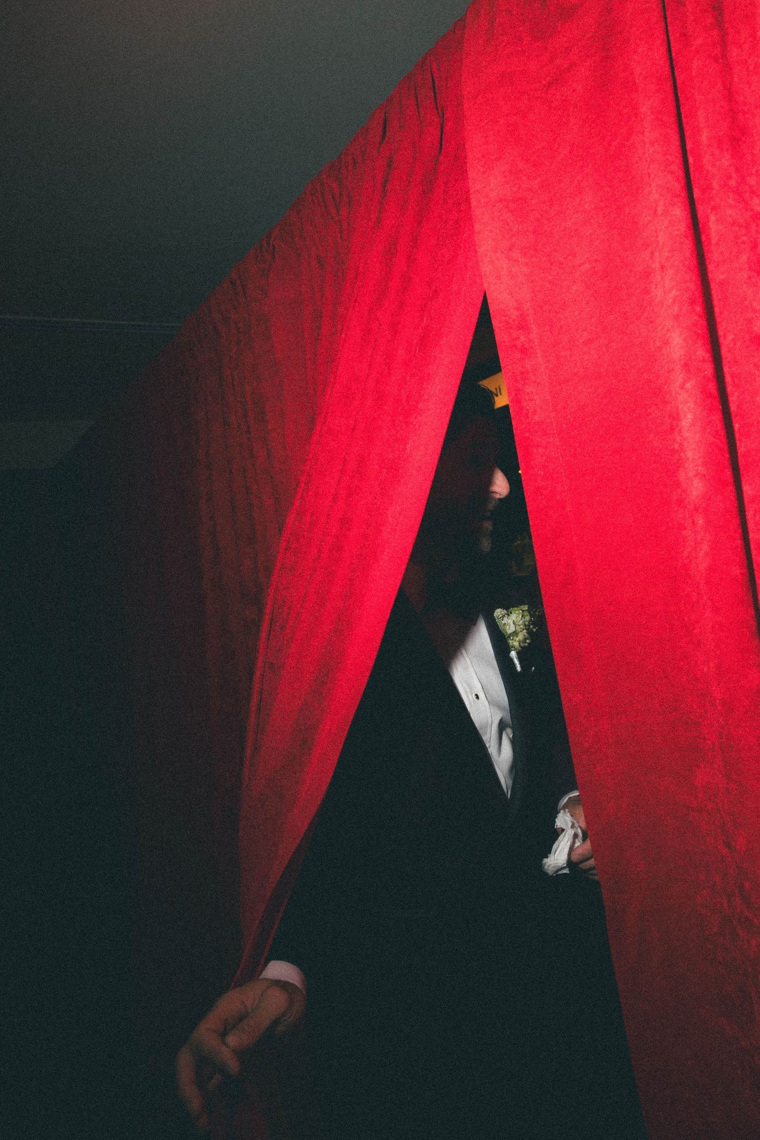 Groom peeks through dramatic red curtains before making his wedding ceremony entrance.