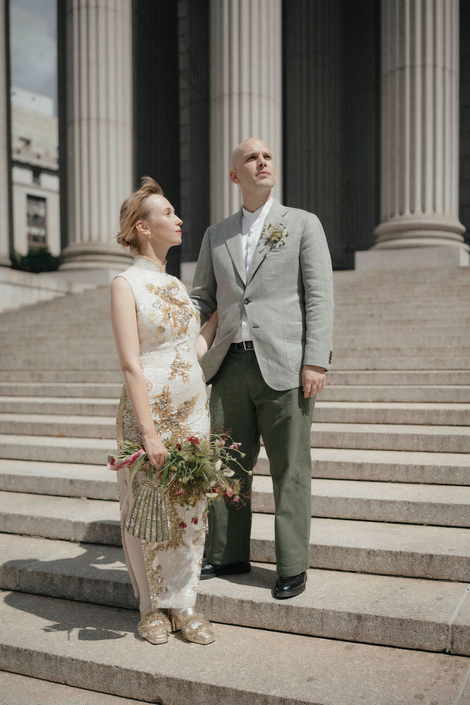 Bride and groom stand on grand stone steps with tall columns in outdoor portrait.