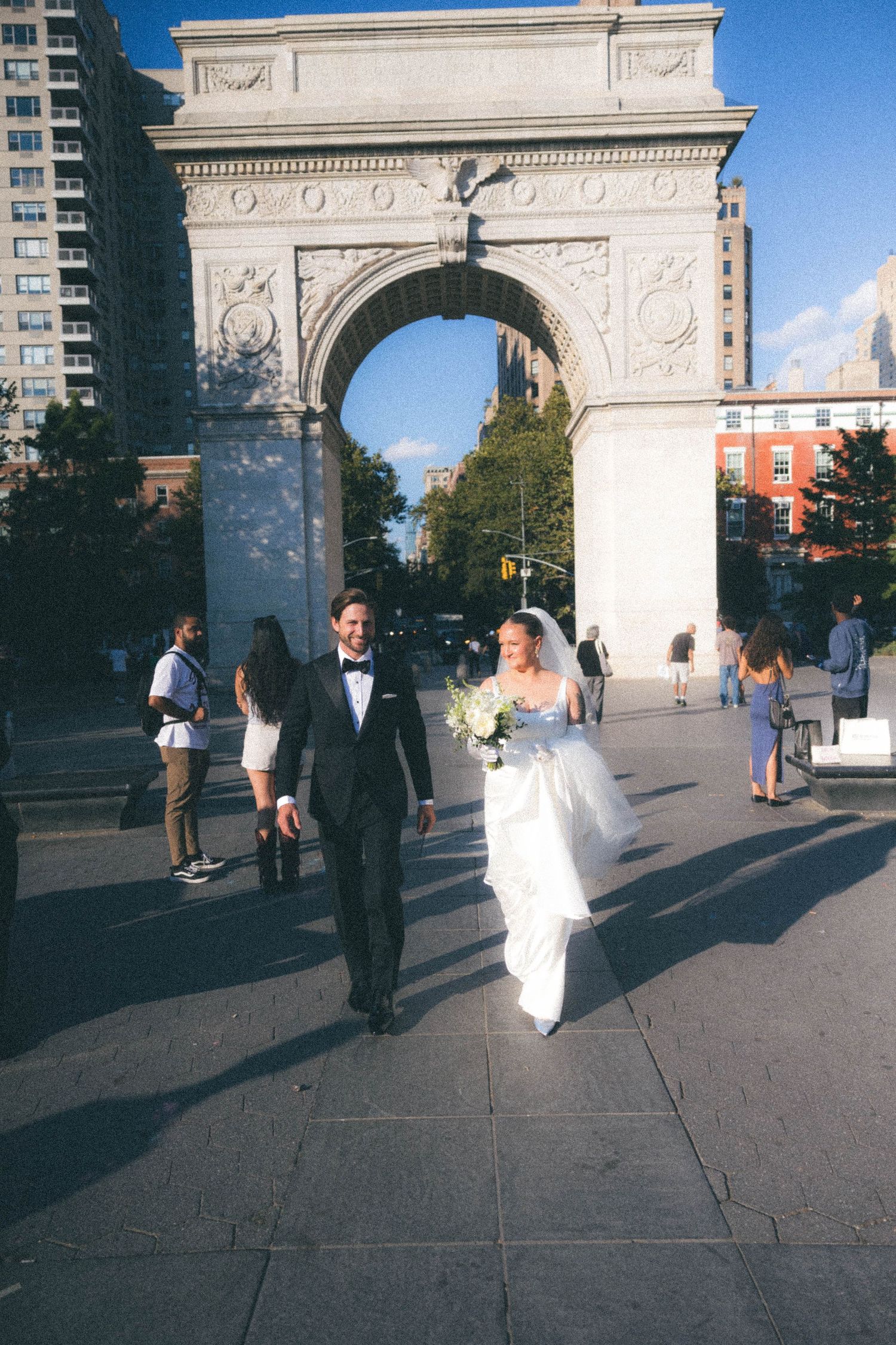 Bride and groom walk hand in hand in front of Washington Square Park arch on their wedding day.