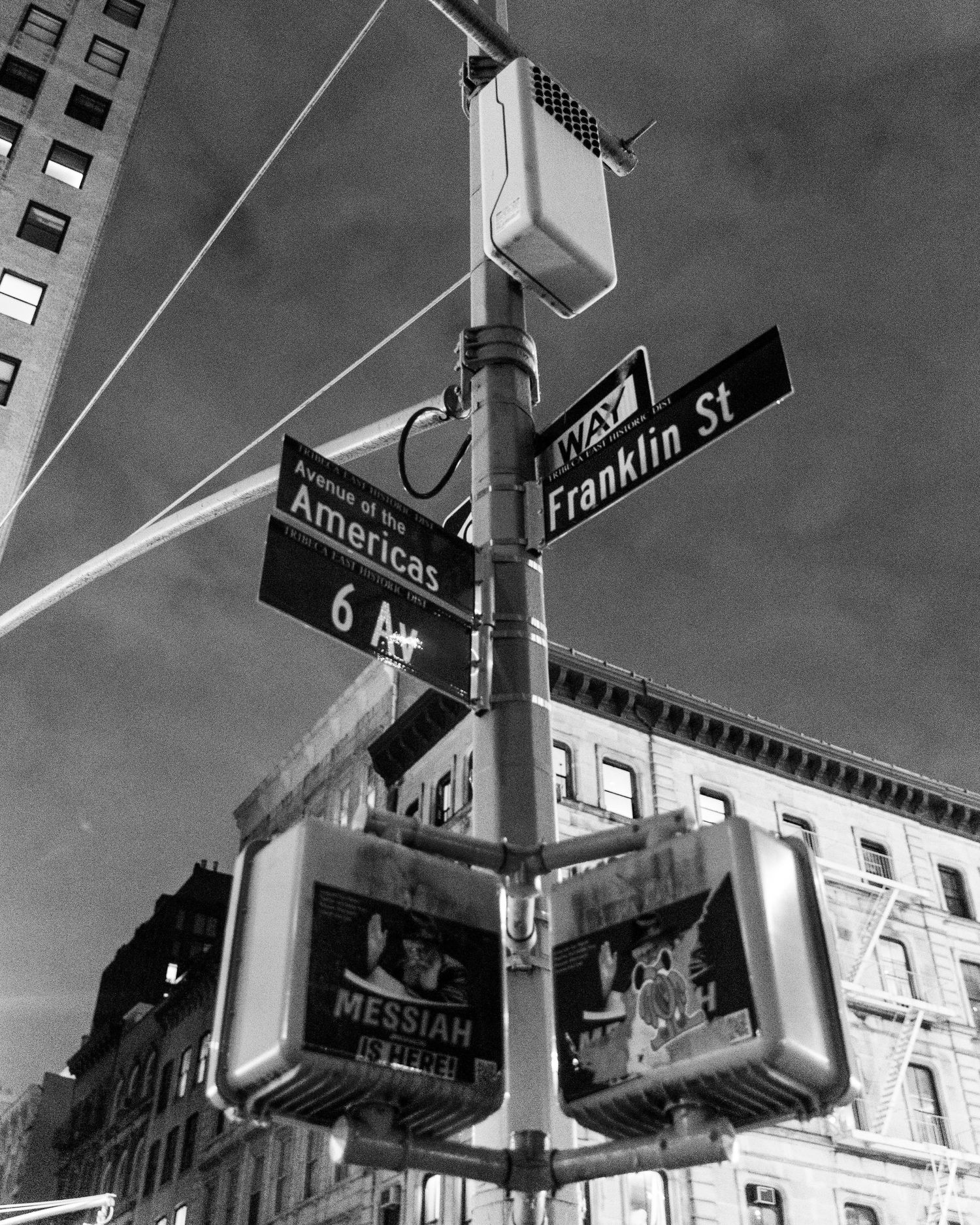 Black and white photo of street signs for Avenue of the Americas and Franklin St on a pole with pedestrian signals in New York City.