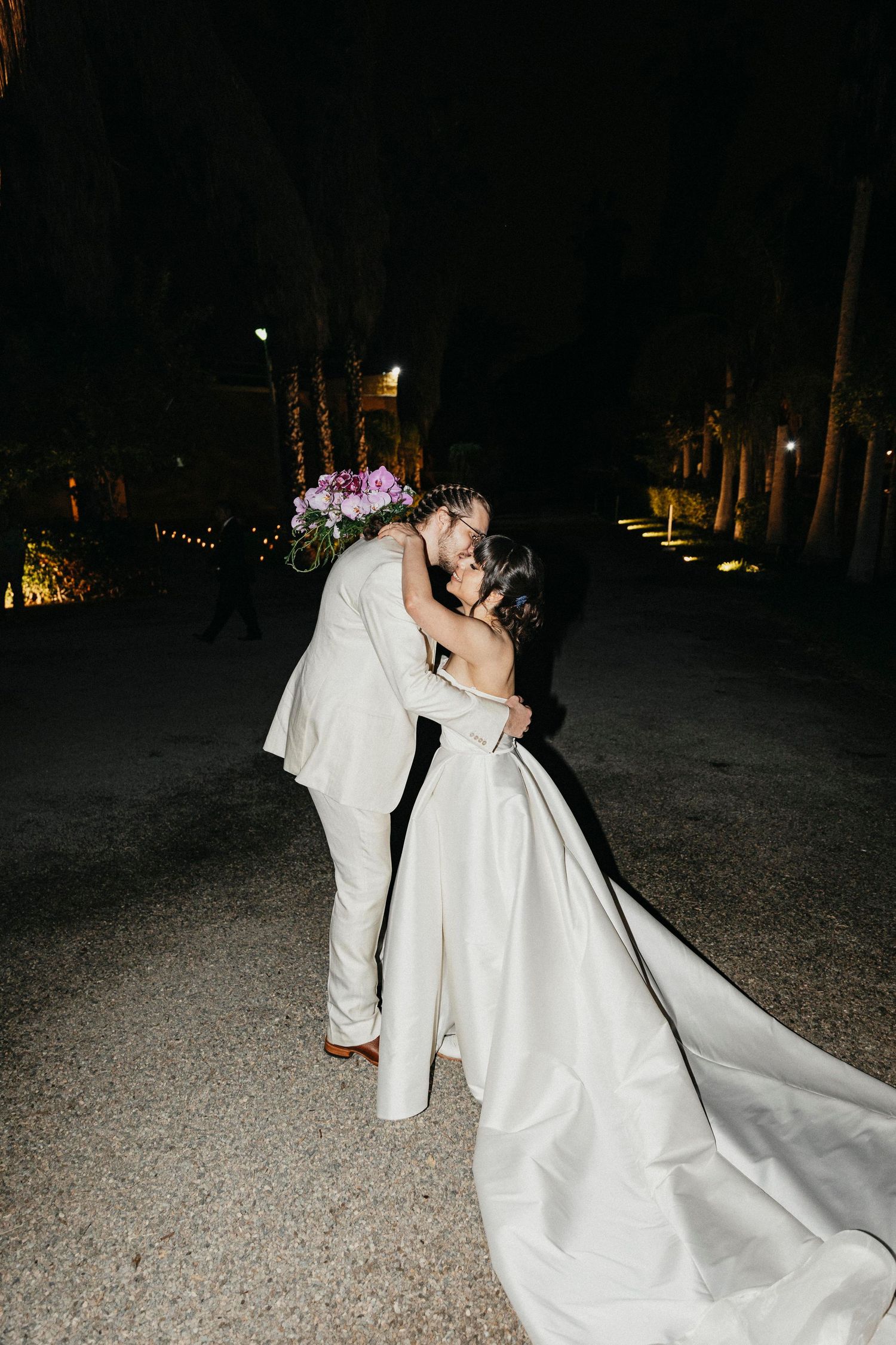 Bride and groom share a romantic dip kiss on a dark outdoor path at their night wedding.