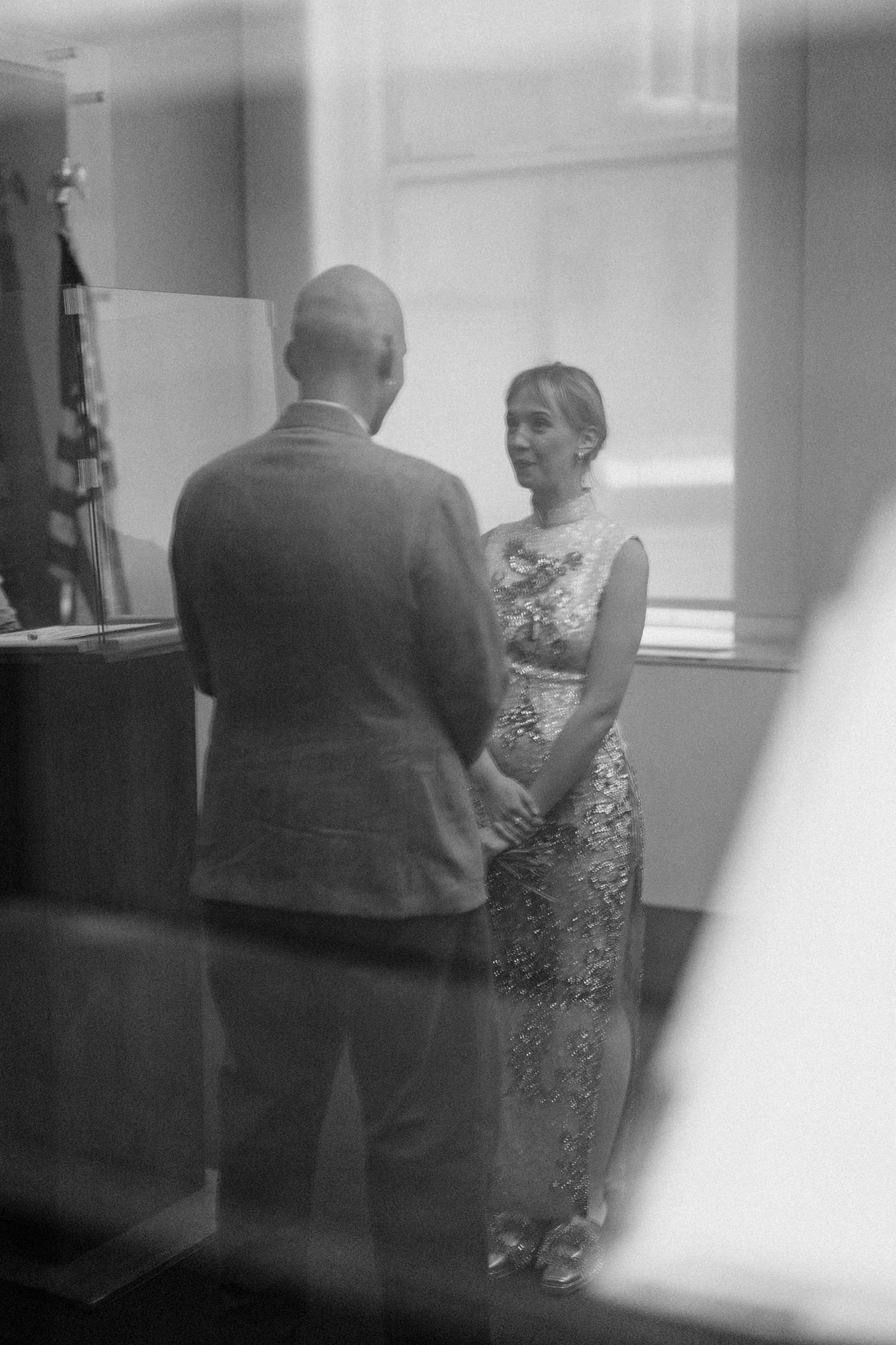 Black and white photo of a couple holding hands during an intimate civil wedding ceremony indoors.
