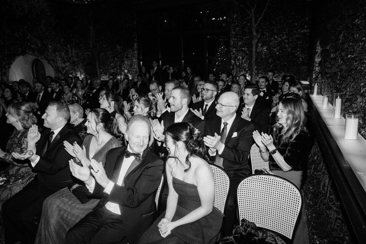 Wedding guests applauding in rows at elegant candlelit reception in black and white photo.