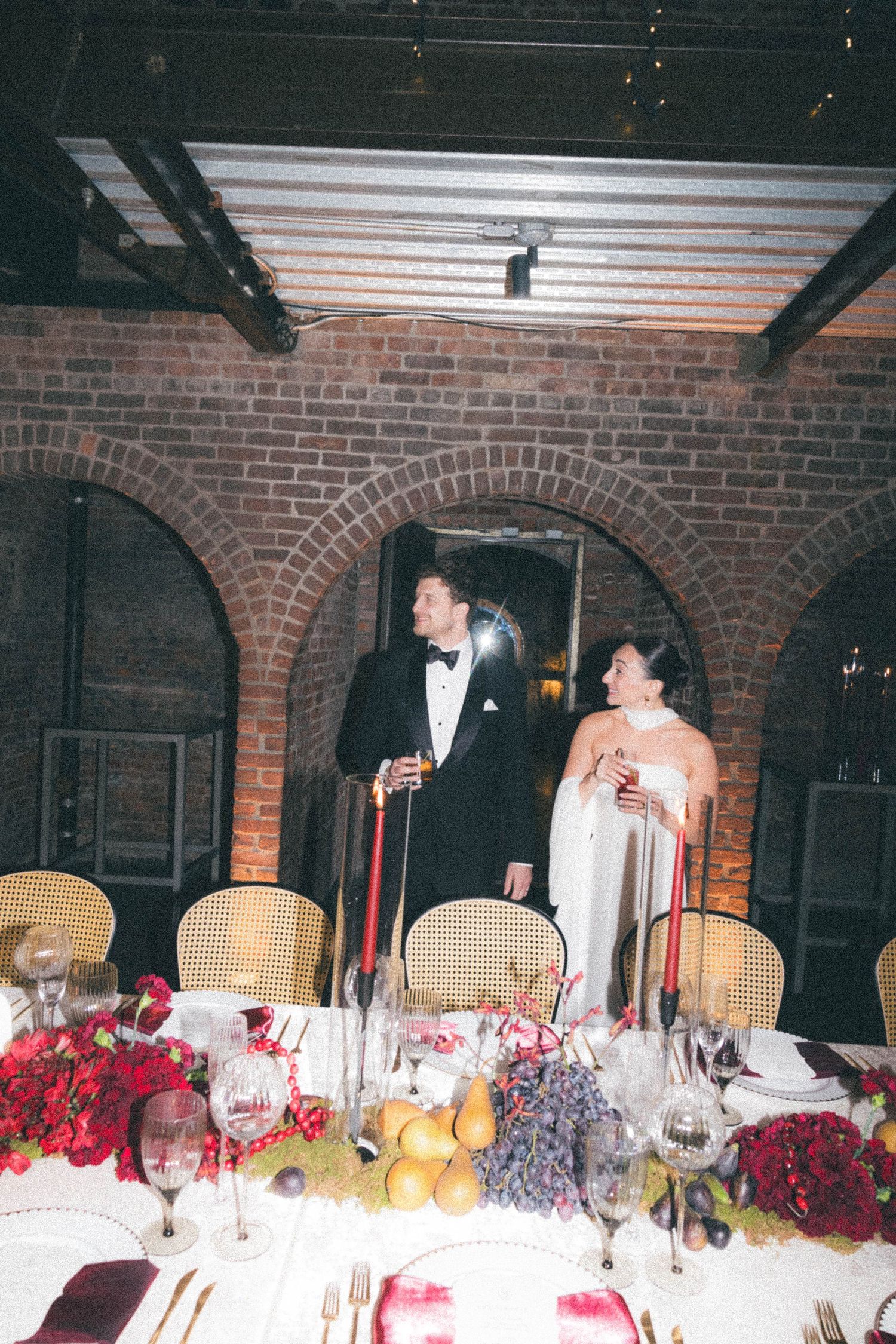 Bride and groom standing together in brick-arched wedding venue with elegant floral table settings.