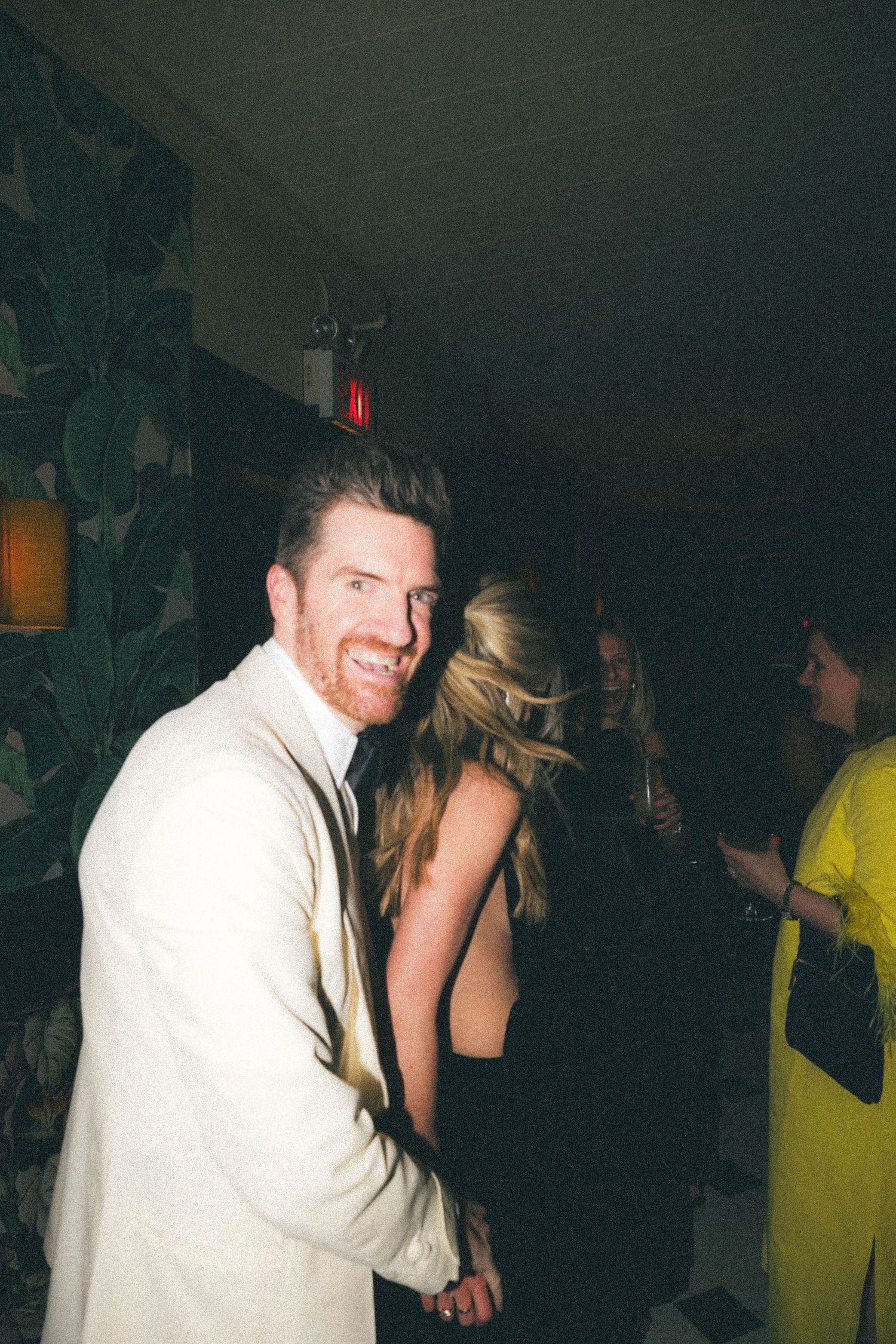 Smiling man in white blazer dancing with woman in backless black dress at elegant evening party.