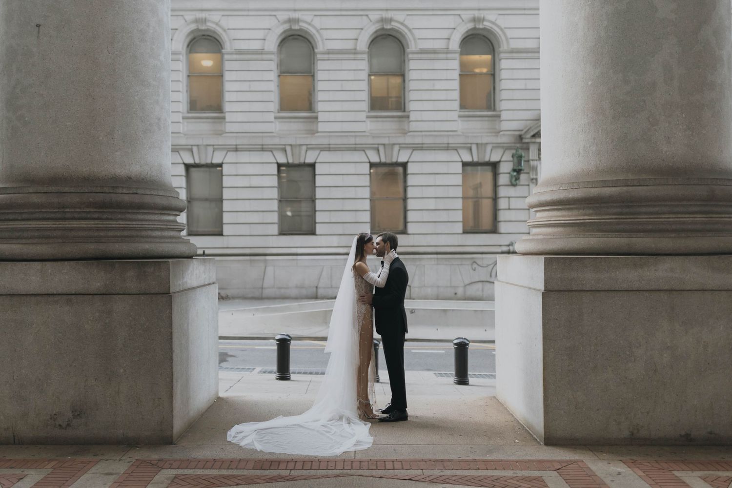 Bride and groom share an intimate moment framed by grand stone columns of a neoclassical building.