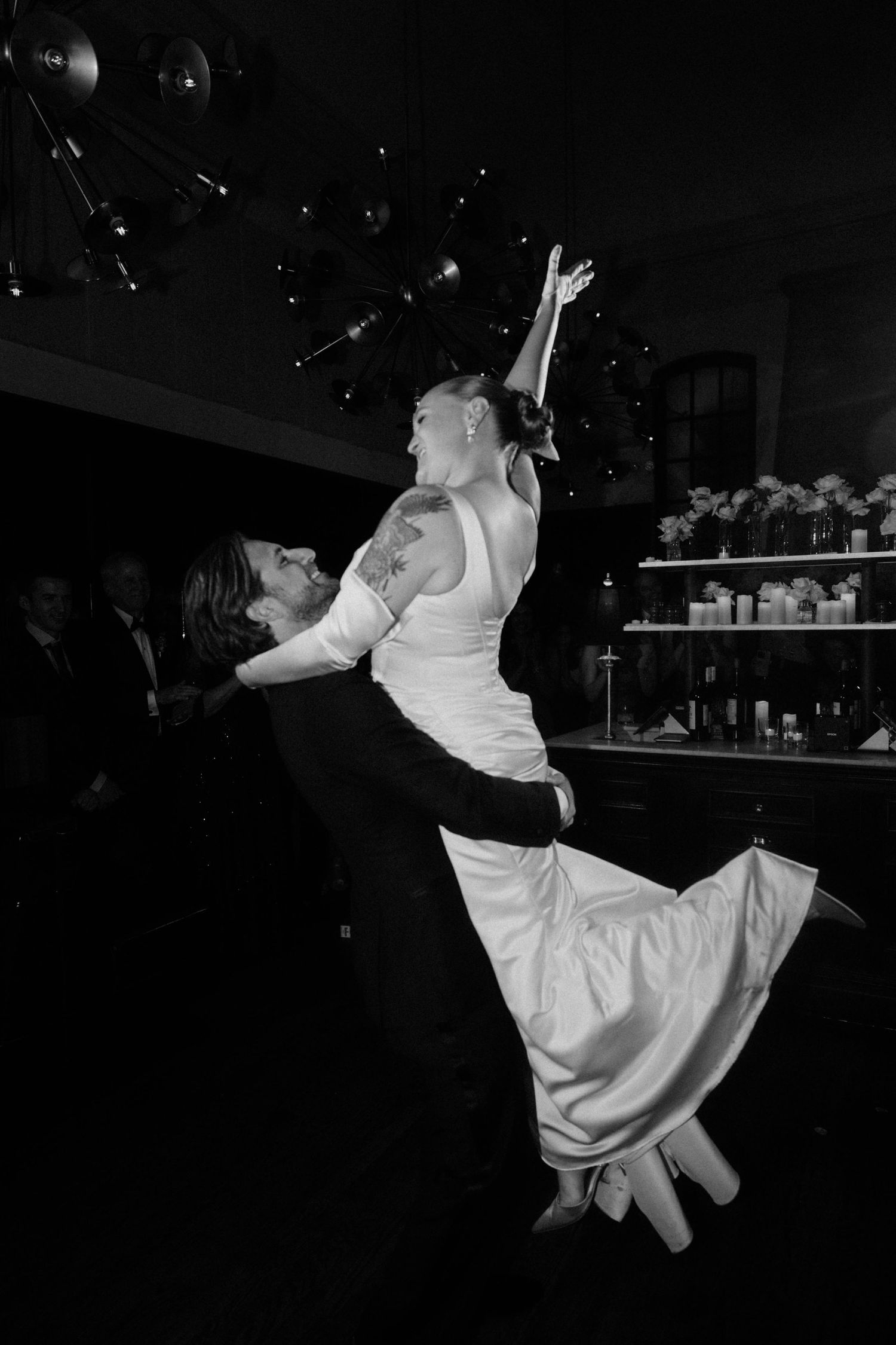 Black and white photo of groom lifting bride during wedding reception dance.