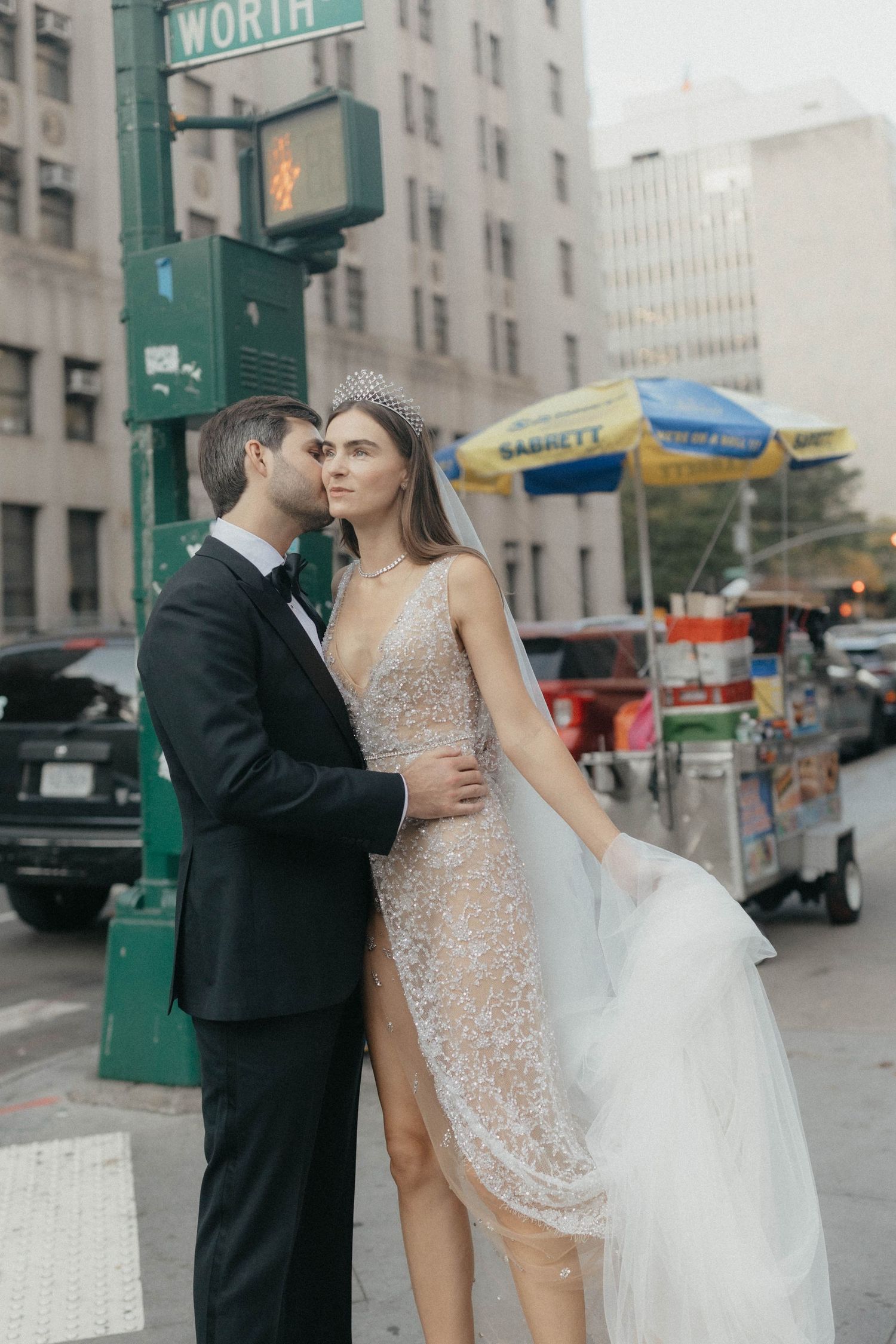 Bride and groom embrace at NYC street corner, bride wearing beaded gown, crystal crown, and flowing veil.