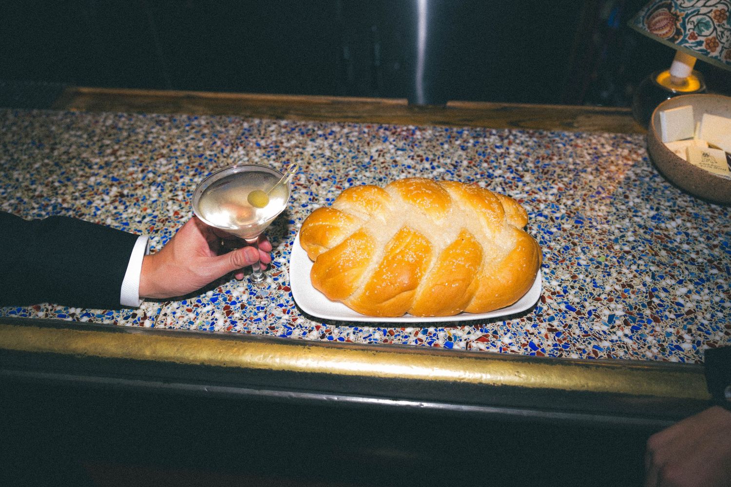 Server presenting a braided challah bread on a white plate at a wedding reception buffet.