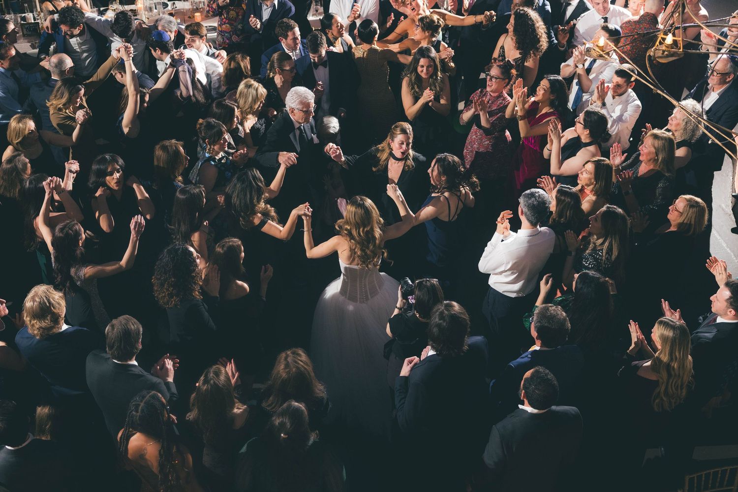 Aerial view of crowded wedding reception dance floor with bride in white gown surrounded by guests.