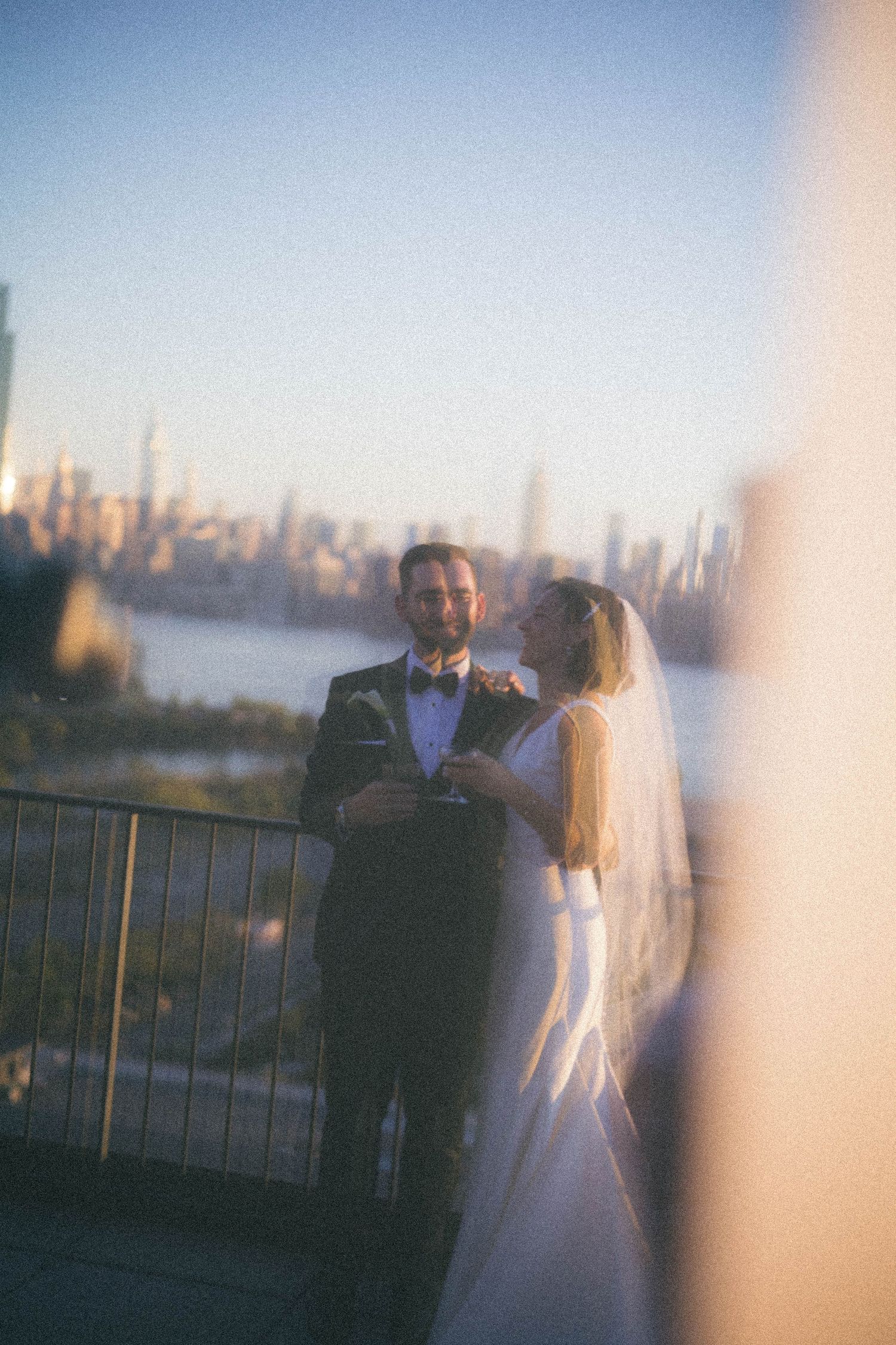 Bride and groom share a romantic moment on a rooftop with the New York City skyline at golden hour.