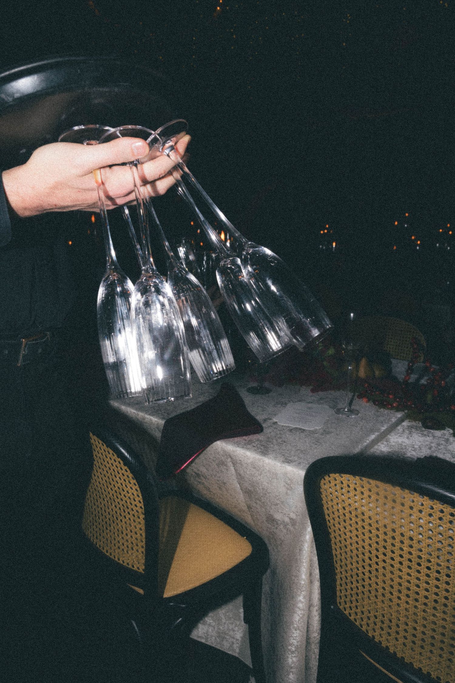 A waiter carries multiple empty wine glasses by their stems at an elegant evening dinner event.