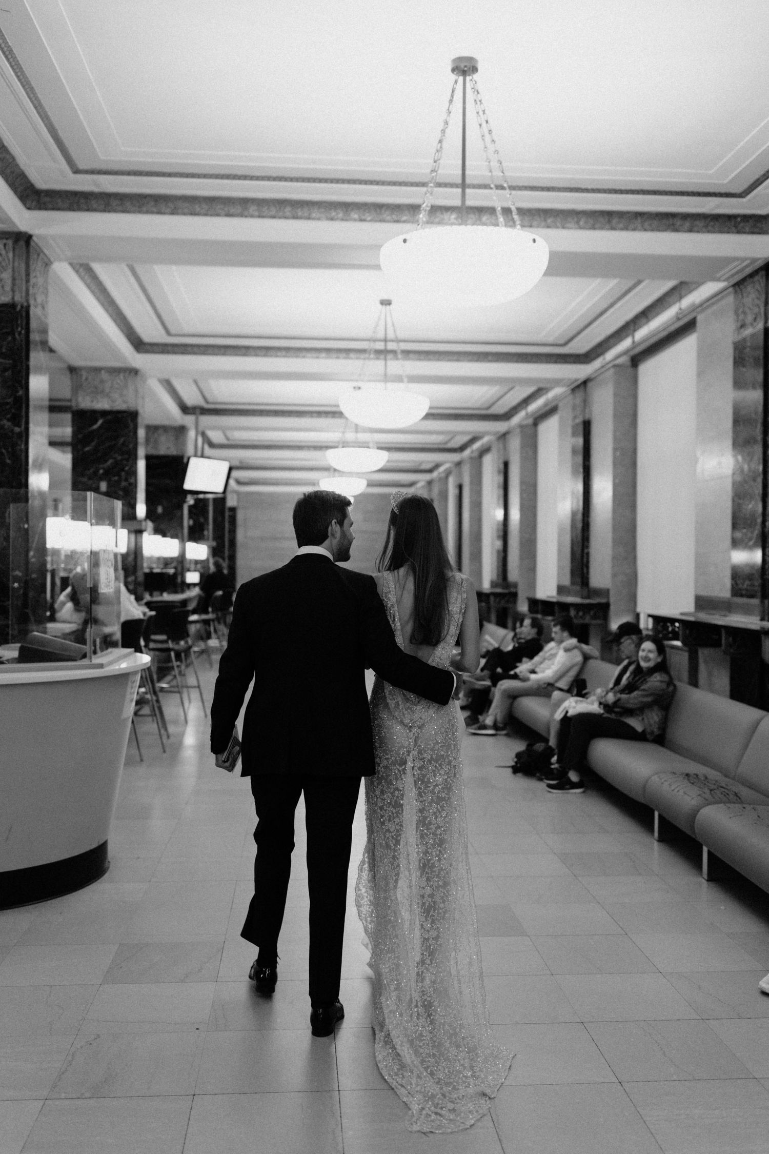 Black and white photo of bride and groom walking hand in hand through an elegant marble hotel lobby.