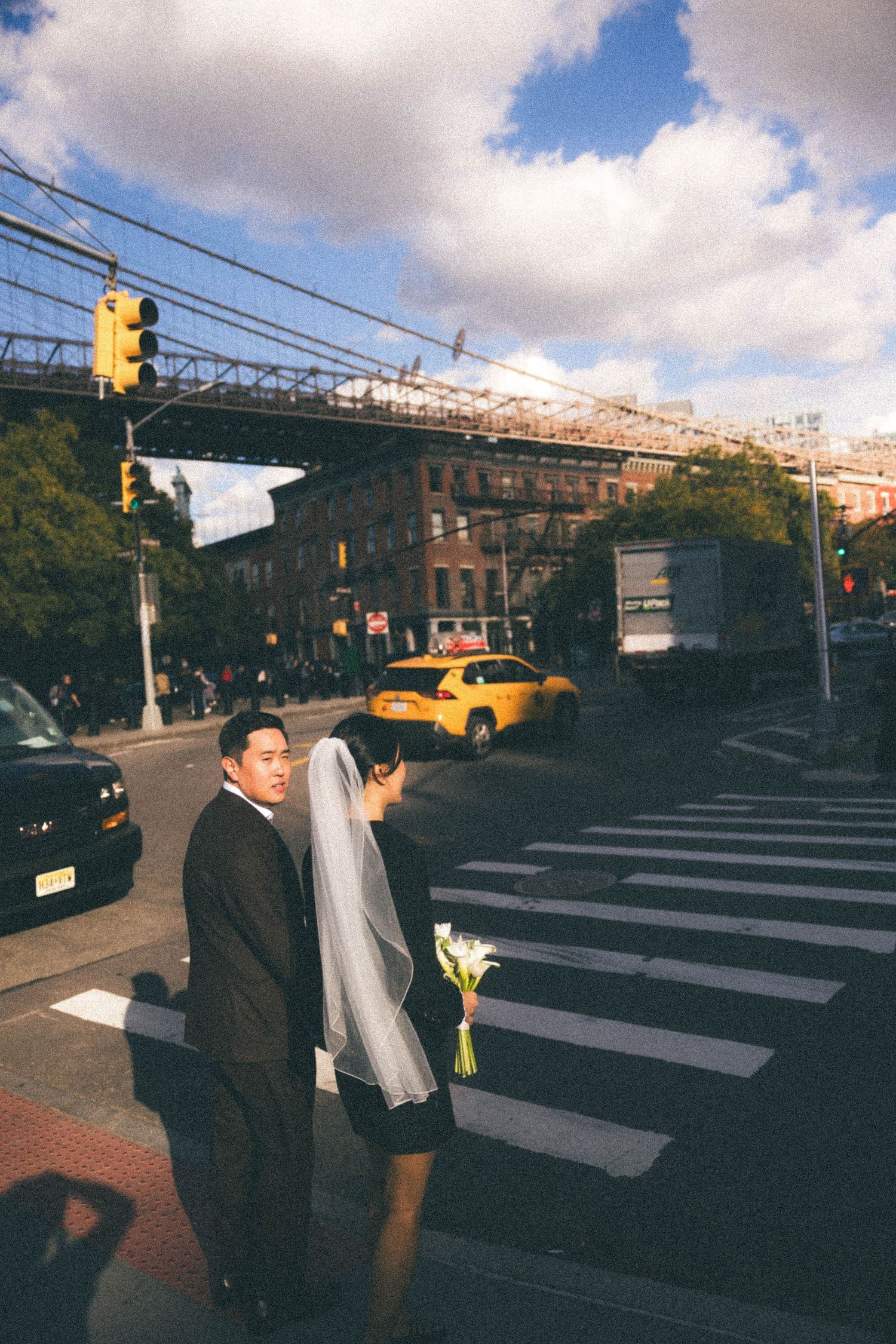 Bride and groom cross busy New York City street intersection on their wedding day.