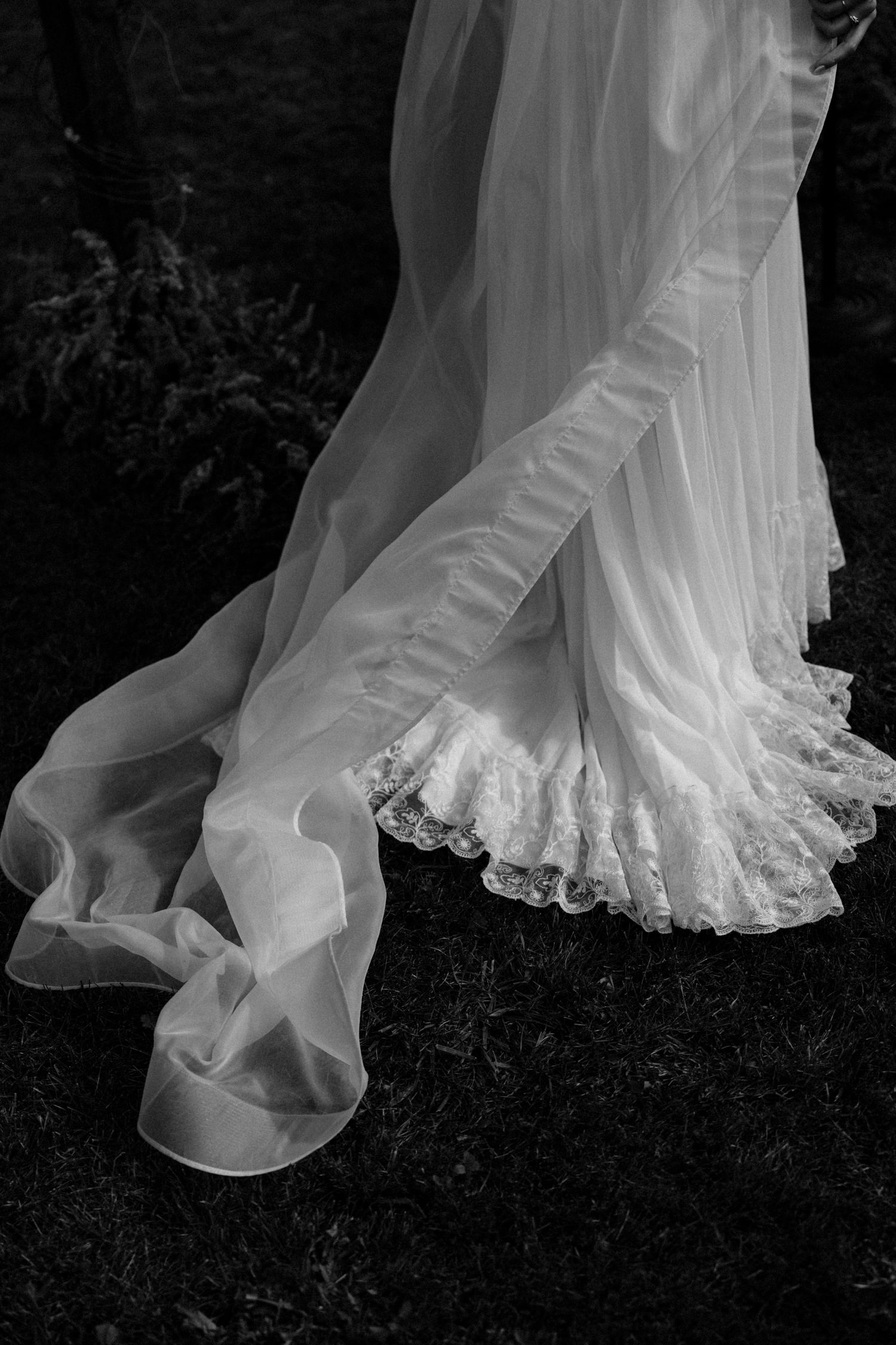Close-up of a flowing white wedding dress with lace trim and sheer veil in black and white photography.