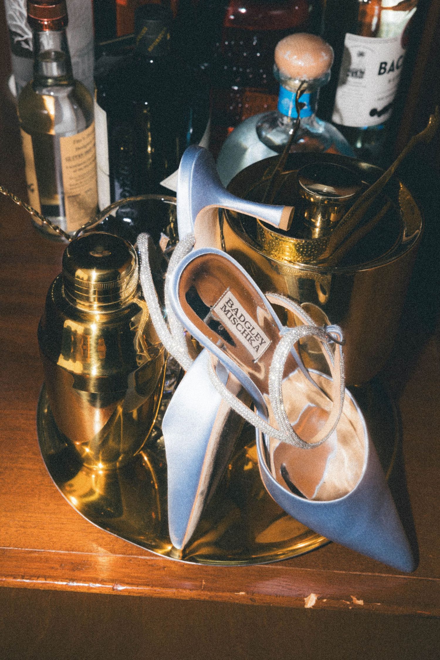 Blue satin Badgley Mischka heels resting on gold tray surrounded by liquor bottles.