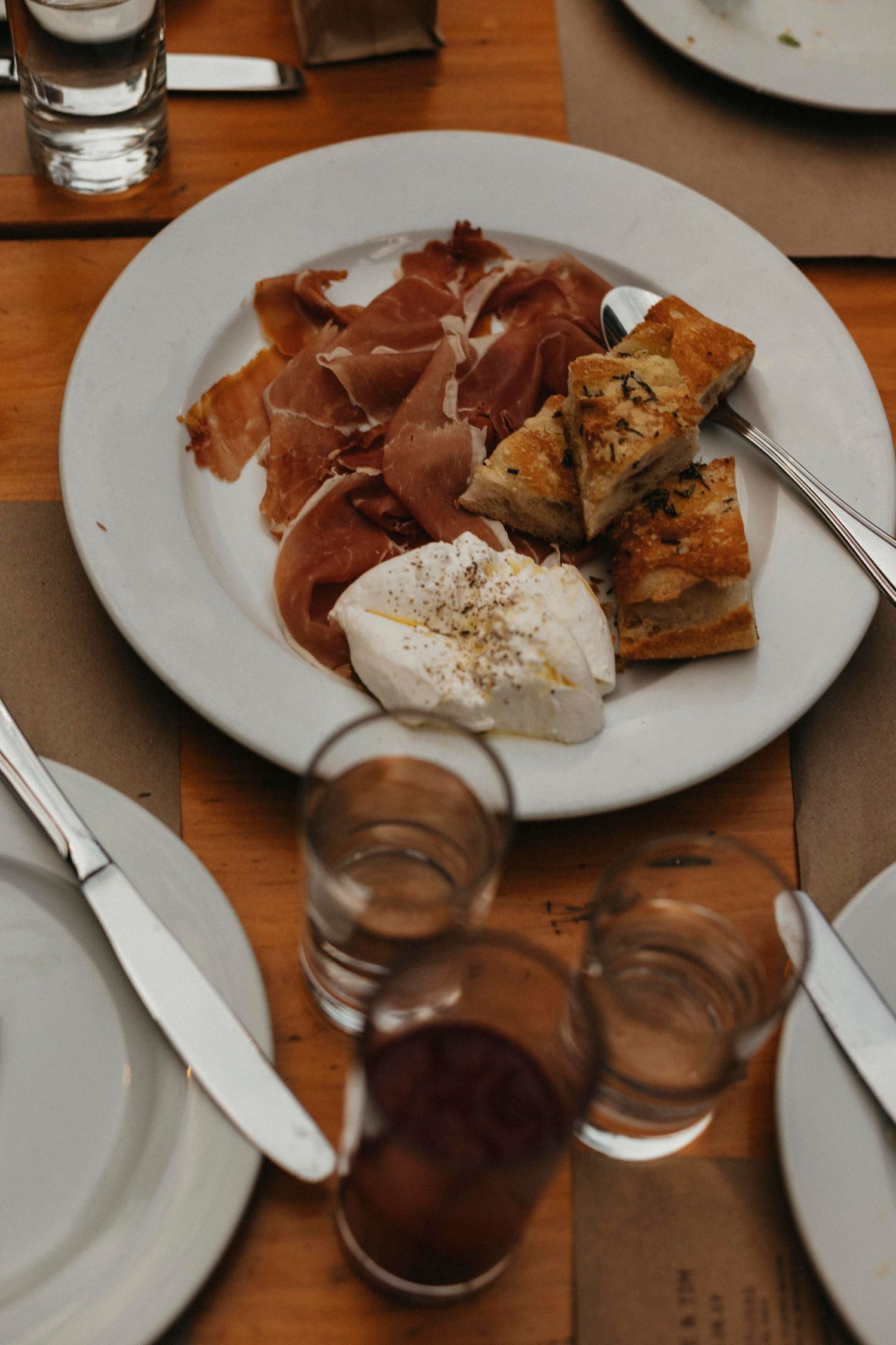 Elegant wedding reception appetizer plate with prosciutto, burrata, and focaccia on rustic wooden table.