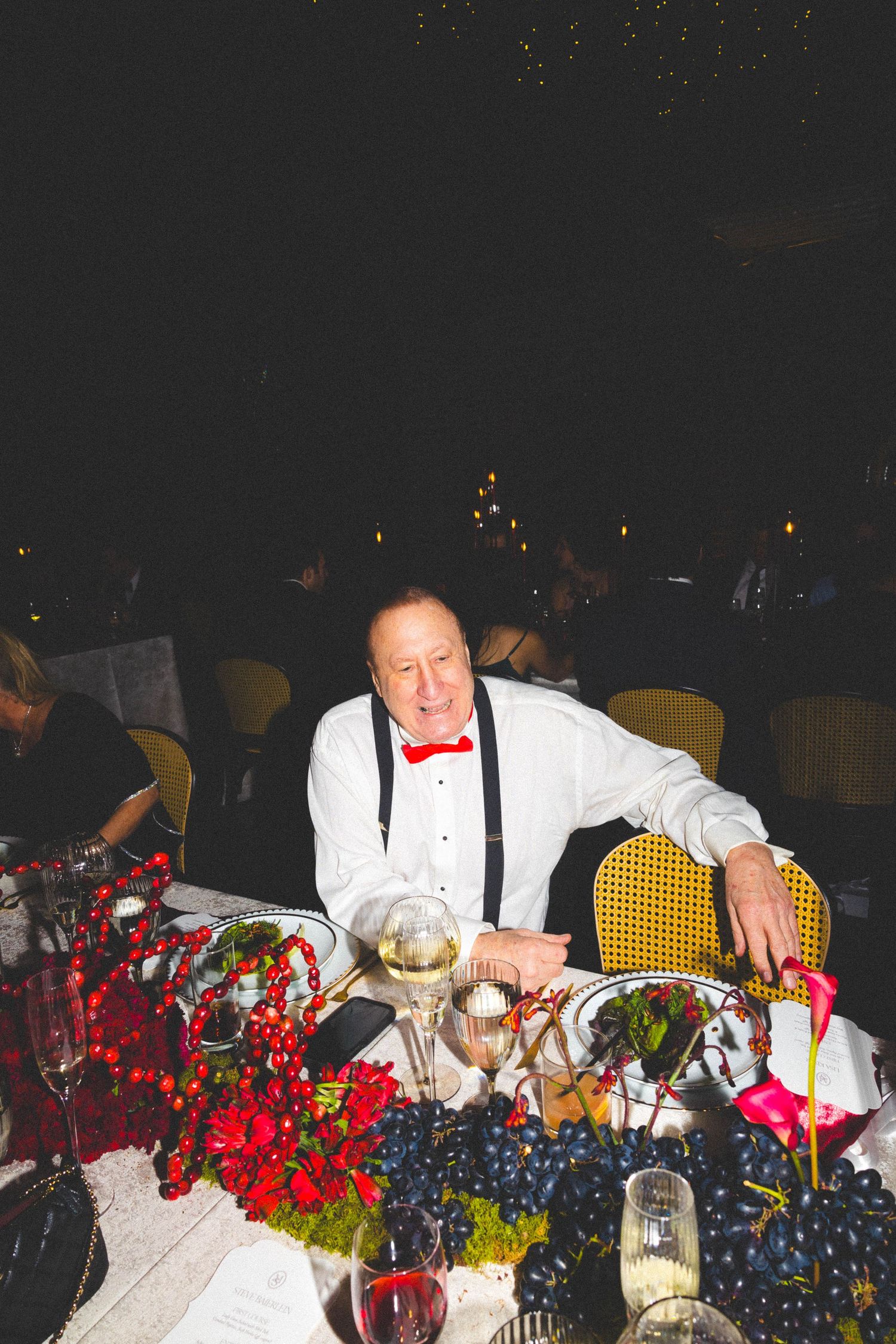 Man in white shirt and red bow tie seated at festive wedding reception dinner table.