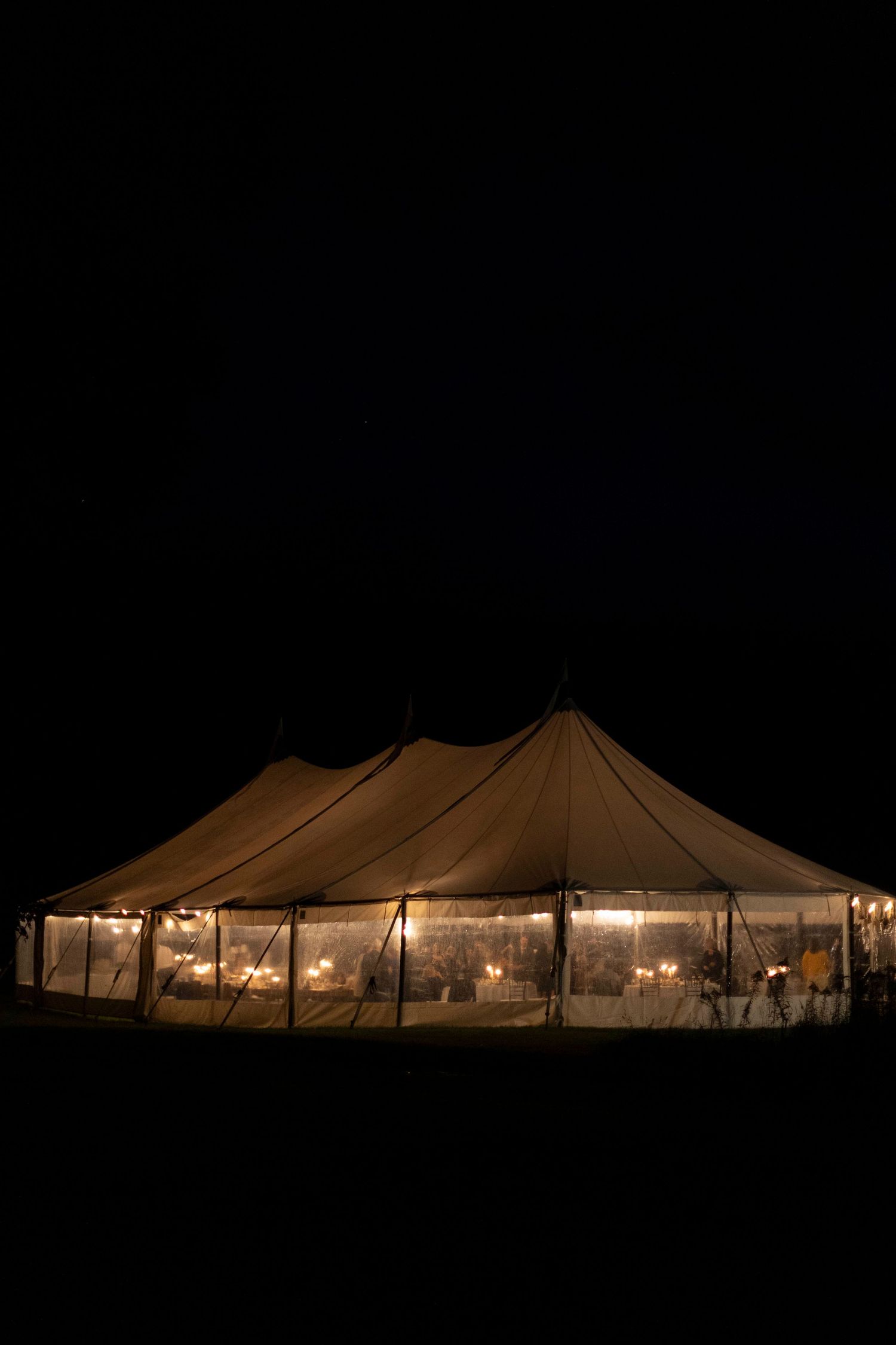 Elegant sailcloth wedding tent glowing warmly with candlelight against dark night sky.