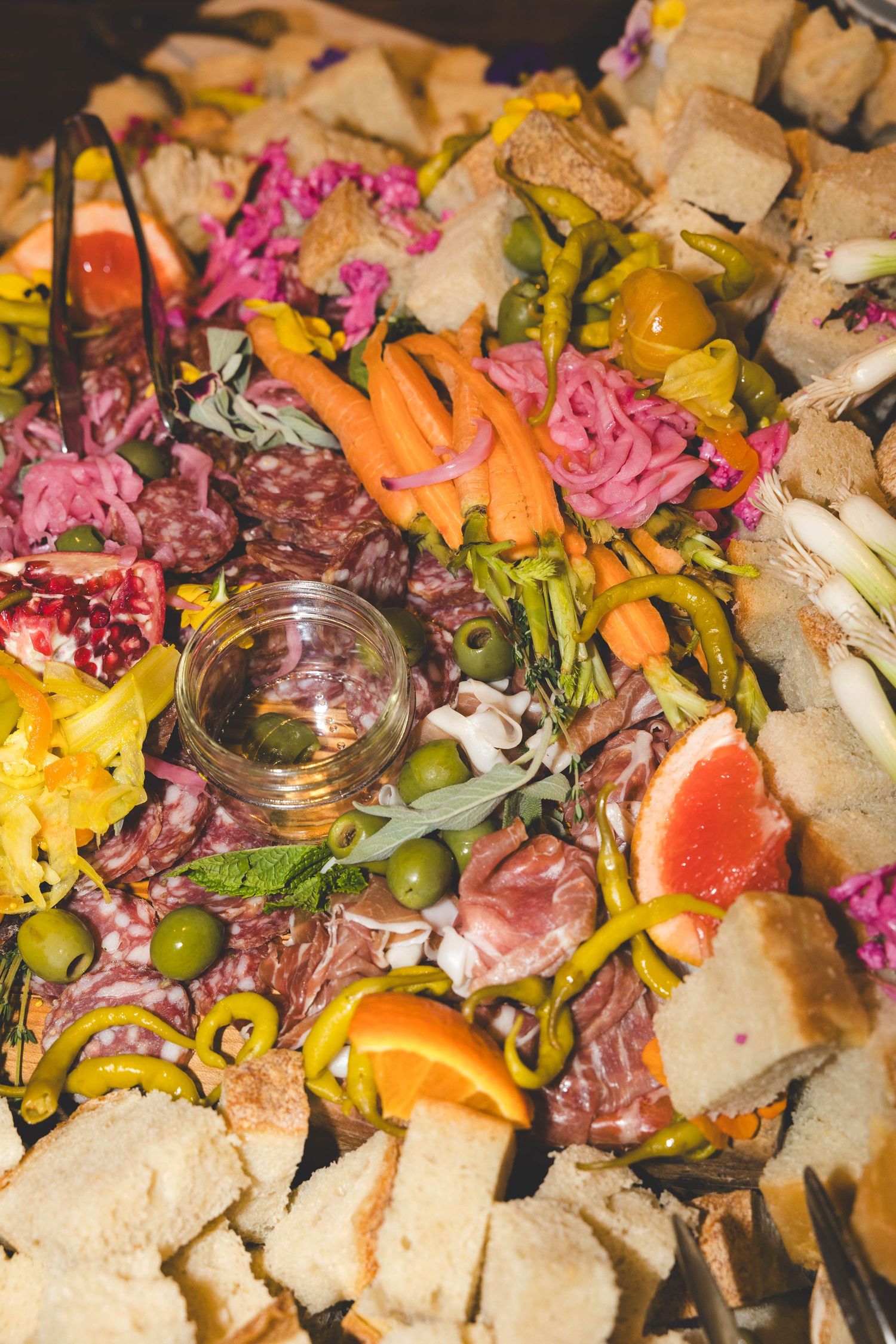Elegant wedding charcuterie board with meats, cheeses, bread, vegetables, olives, and colorful garnishes.