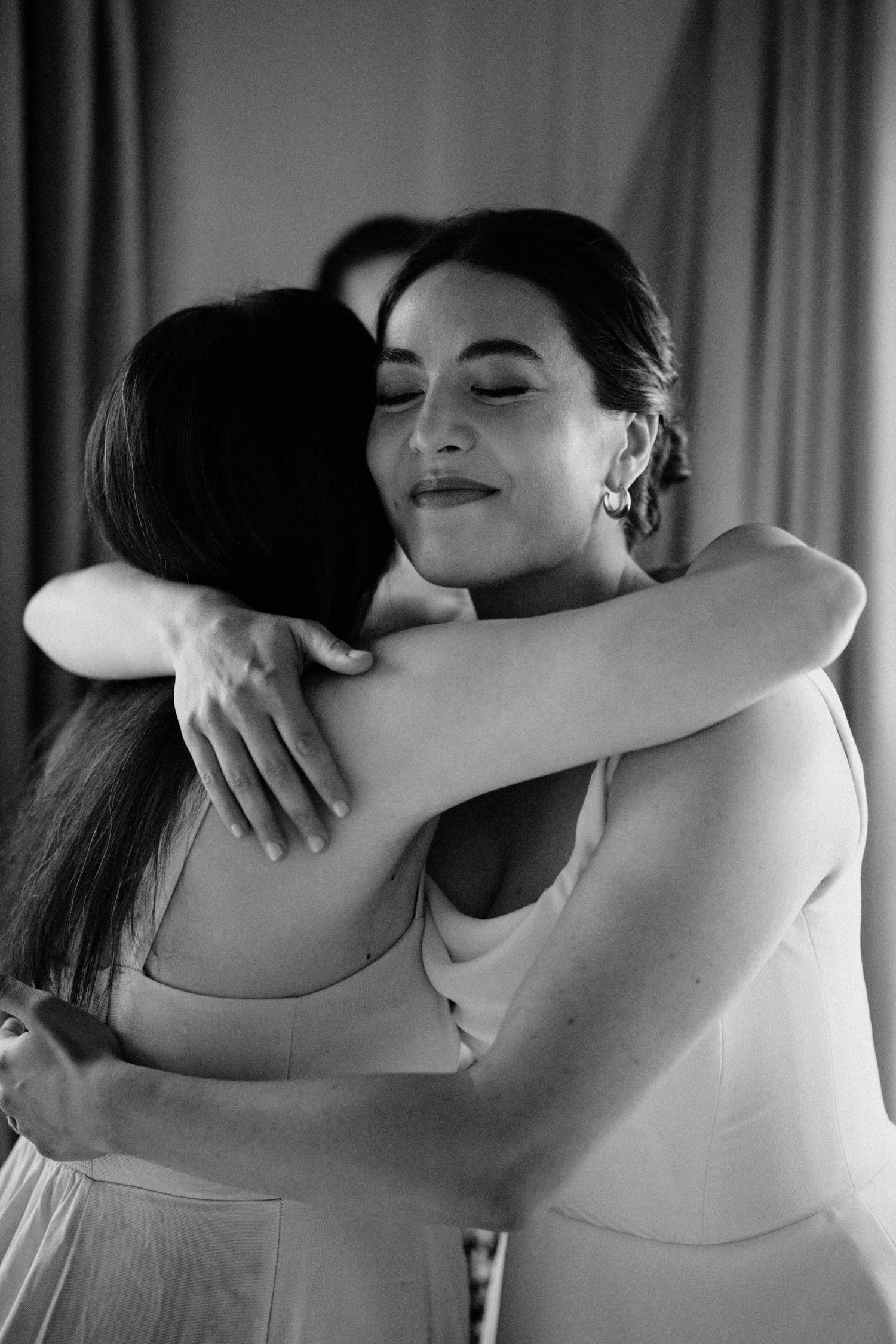 Bride shares a heartfelt embrace with a guest in an elegant black and white portrait.