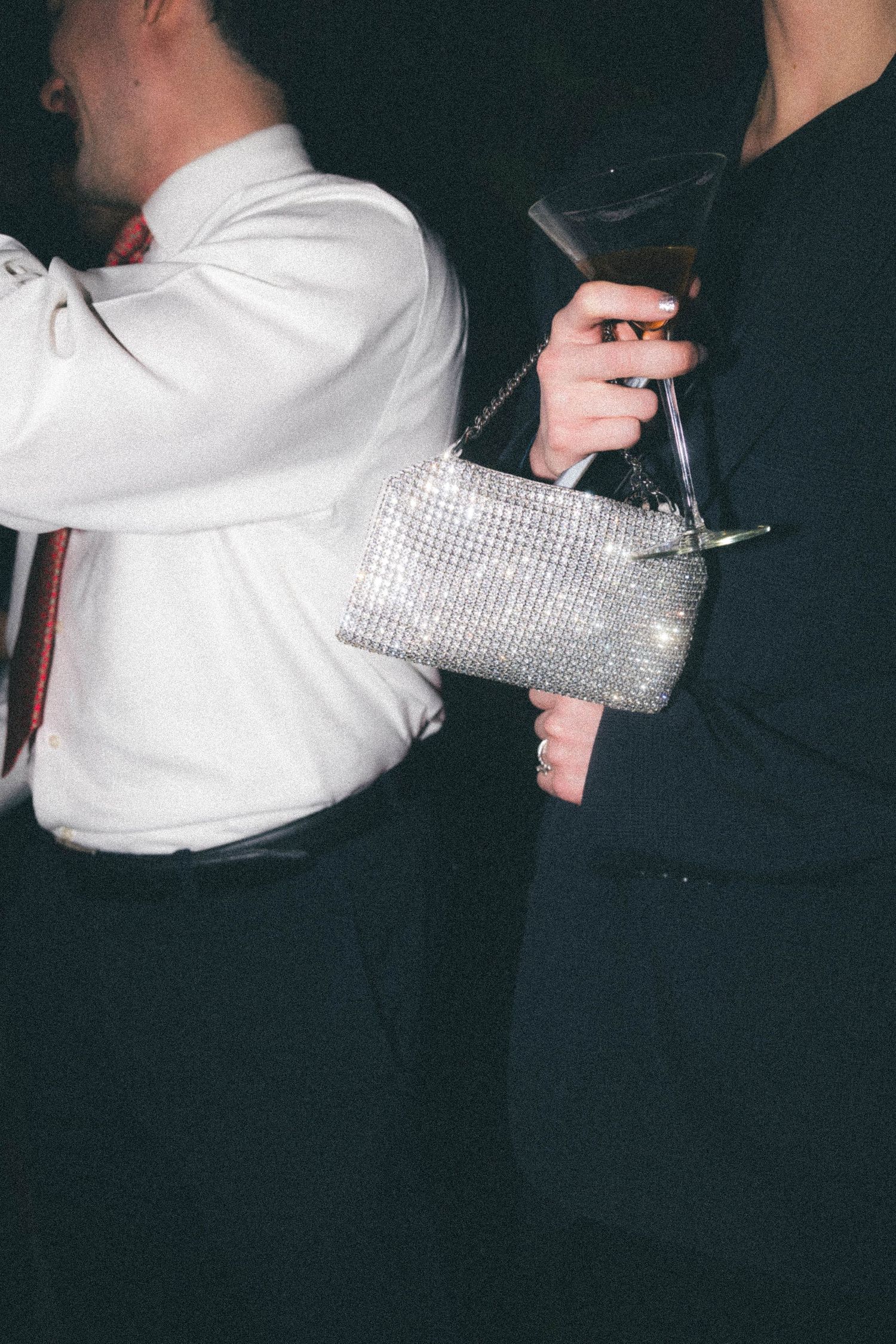 Close-up of woman holding sparkling rhinestone clutch and champagne glass at formal evening event.