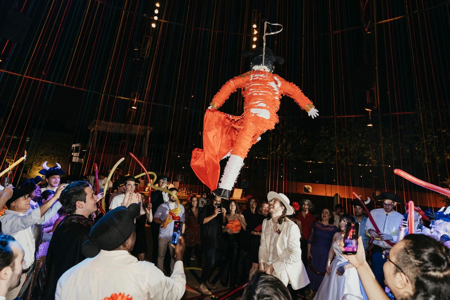 Giant astronaut pinata bursts open above cheering wedding guests at a vibrant outdoor evening reception.