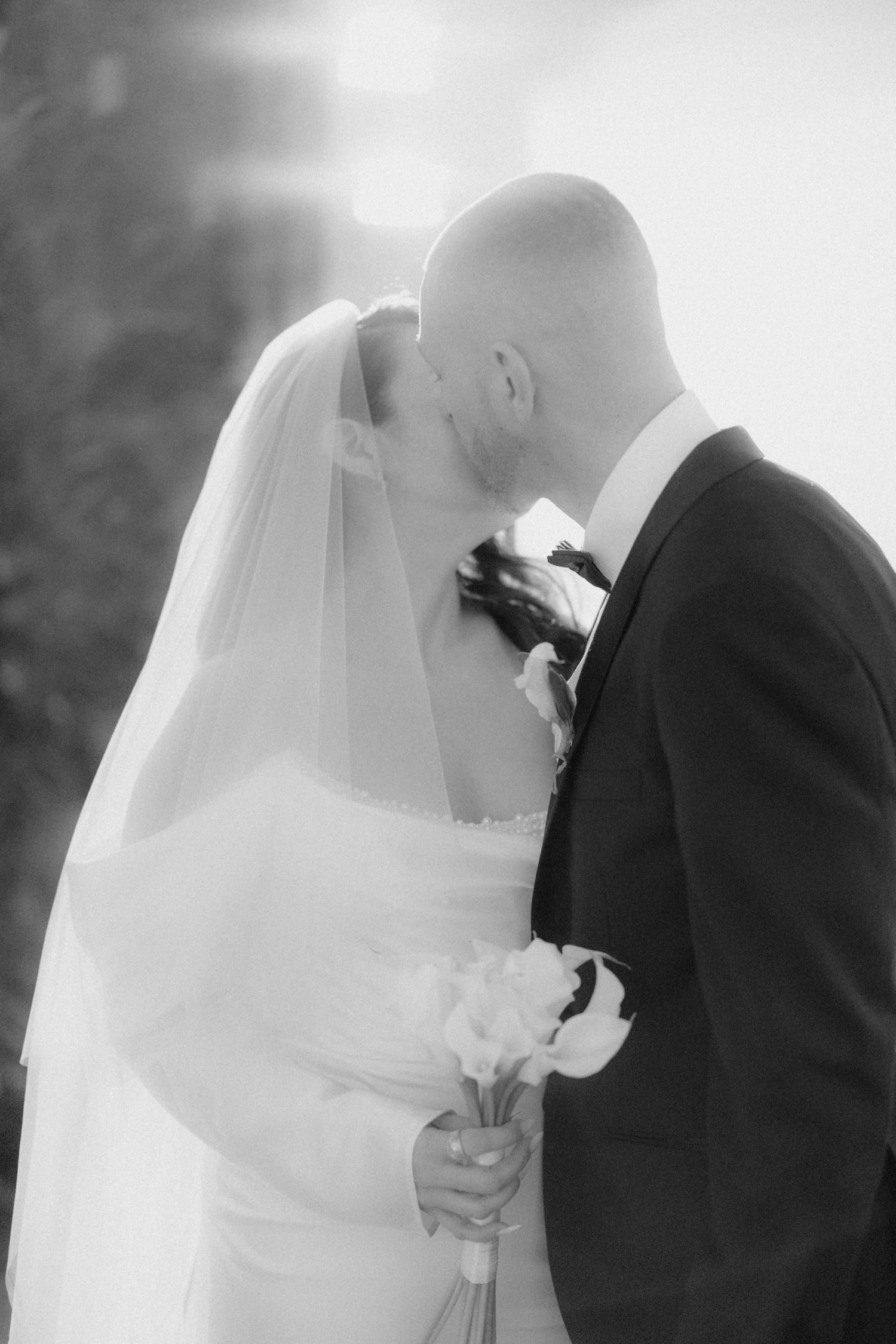 Black and white romantic photo of bride and groom sharing first kiss at outdoor wedding.