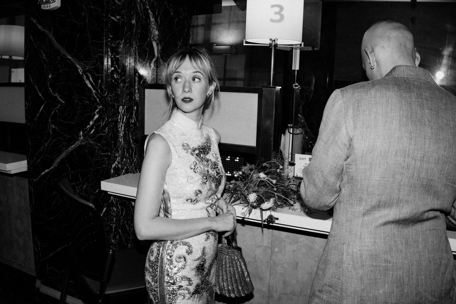 Black and white candid photo of blonde bride holding floral bouquet at a reception desk.
