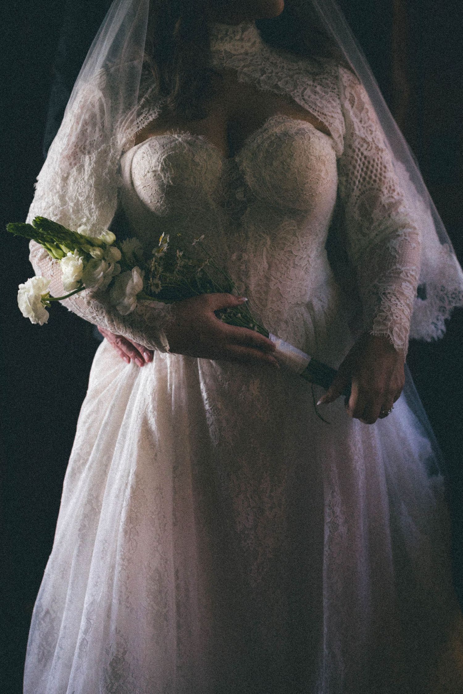 Bride in lace long-sleeve wedding gown holding white floral bouquet with veil.