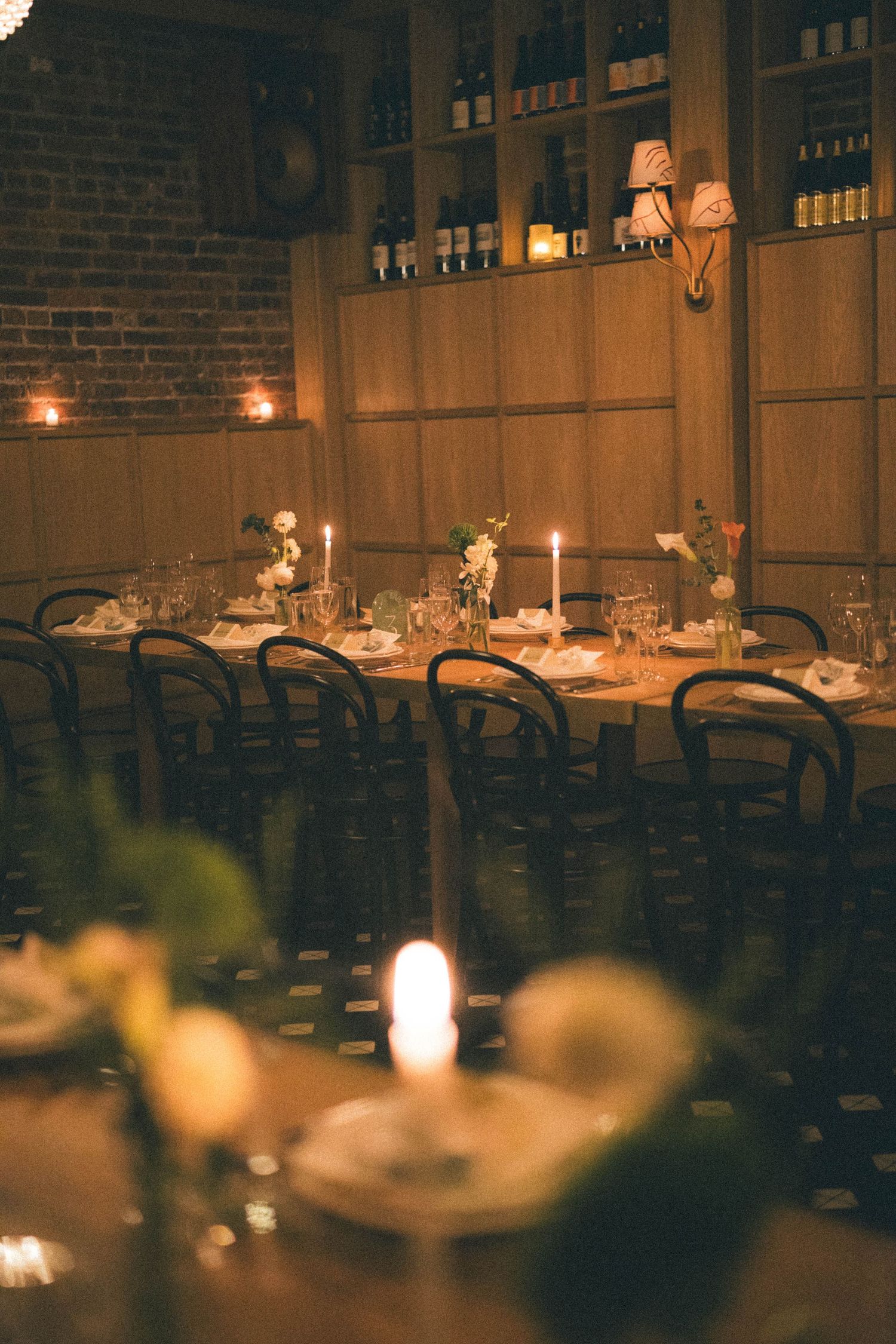 Candlelit wedding reception dinner table with elegant floral arrangements in a warm, rustic restaurant setting.