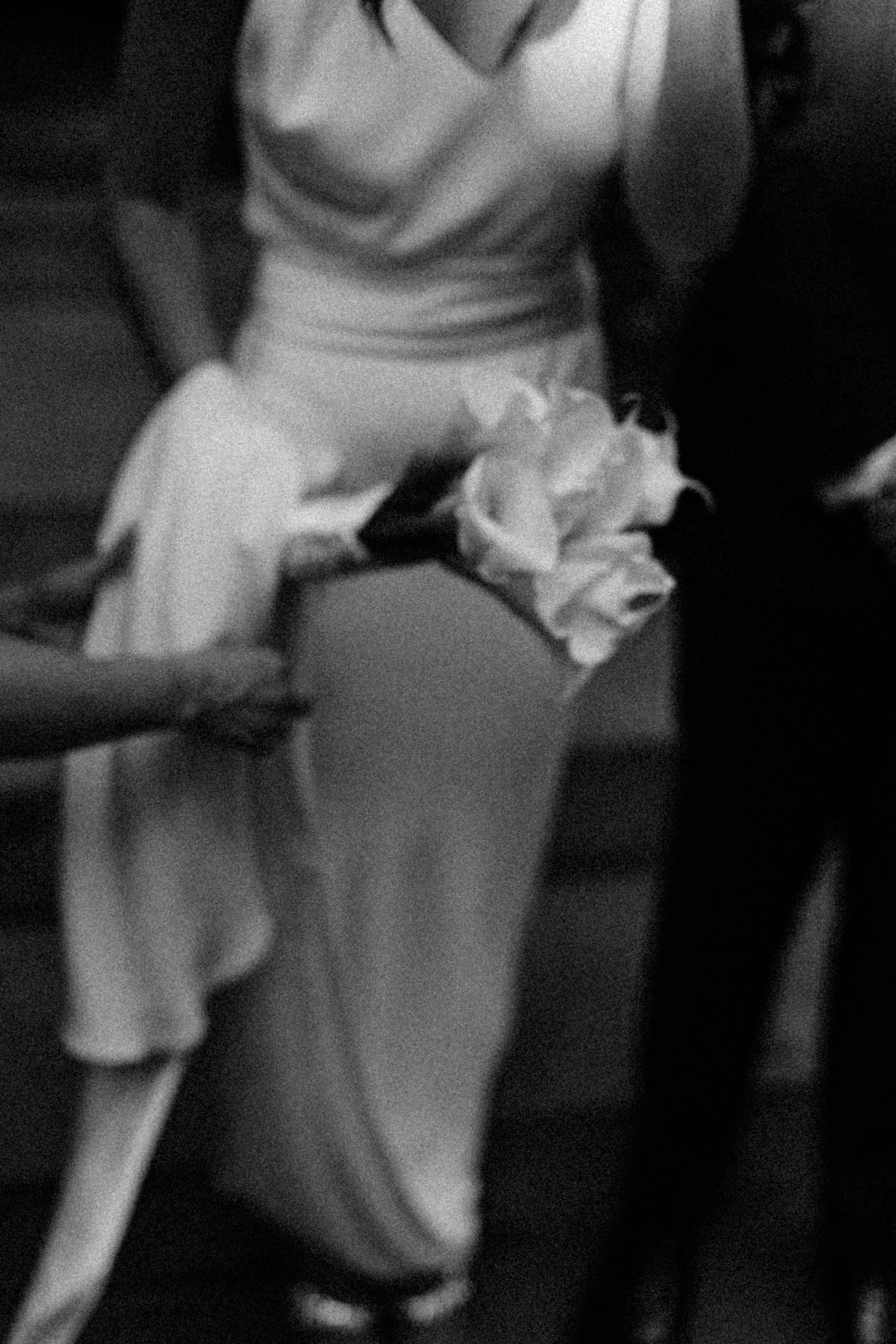 Black and white close-up of bride in white gown holding a single rose bouquet at wedding ceremony.