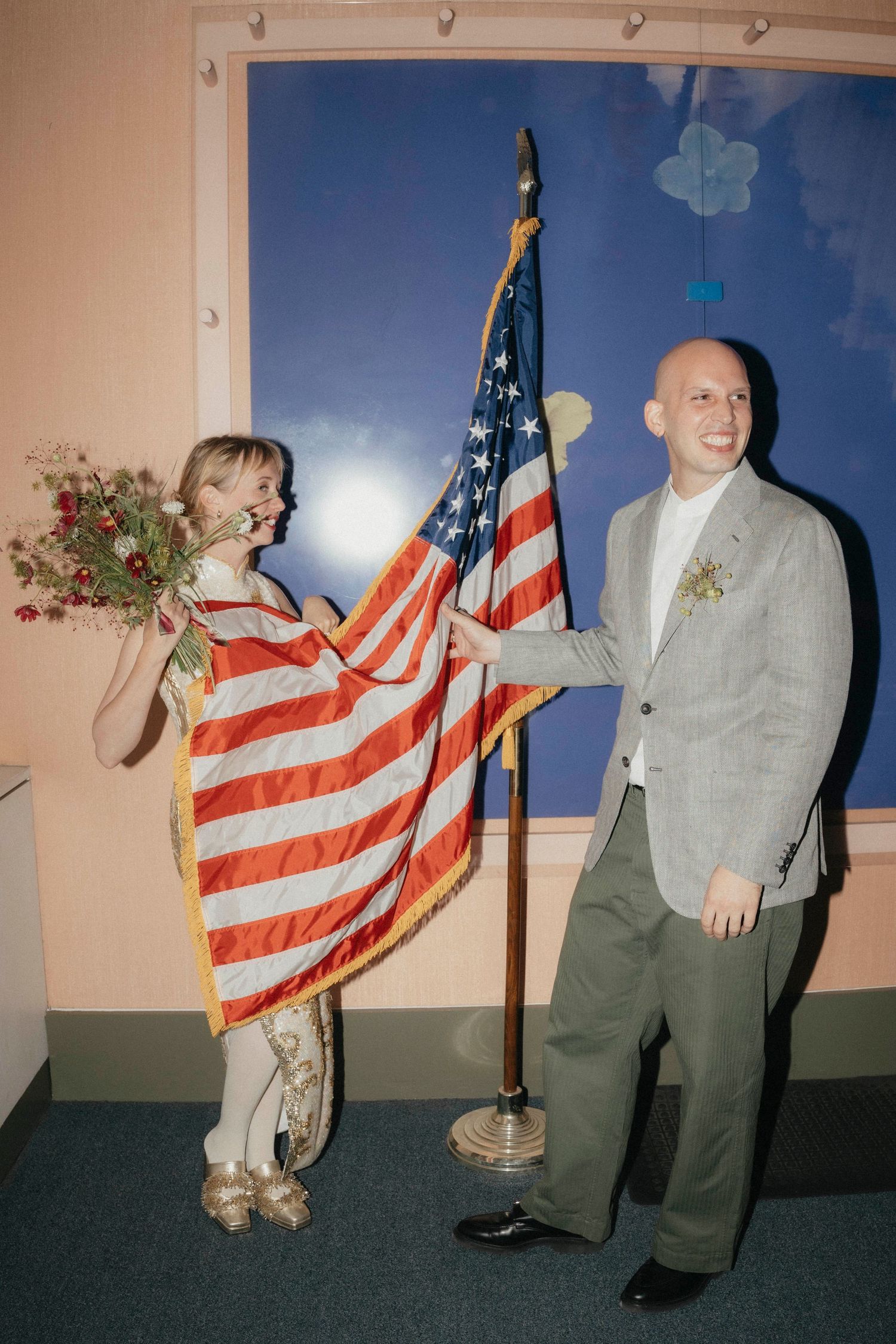 Smiling couple posing with an American flag in a colorful room after courthouse wedding.