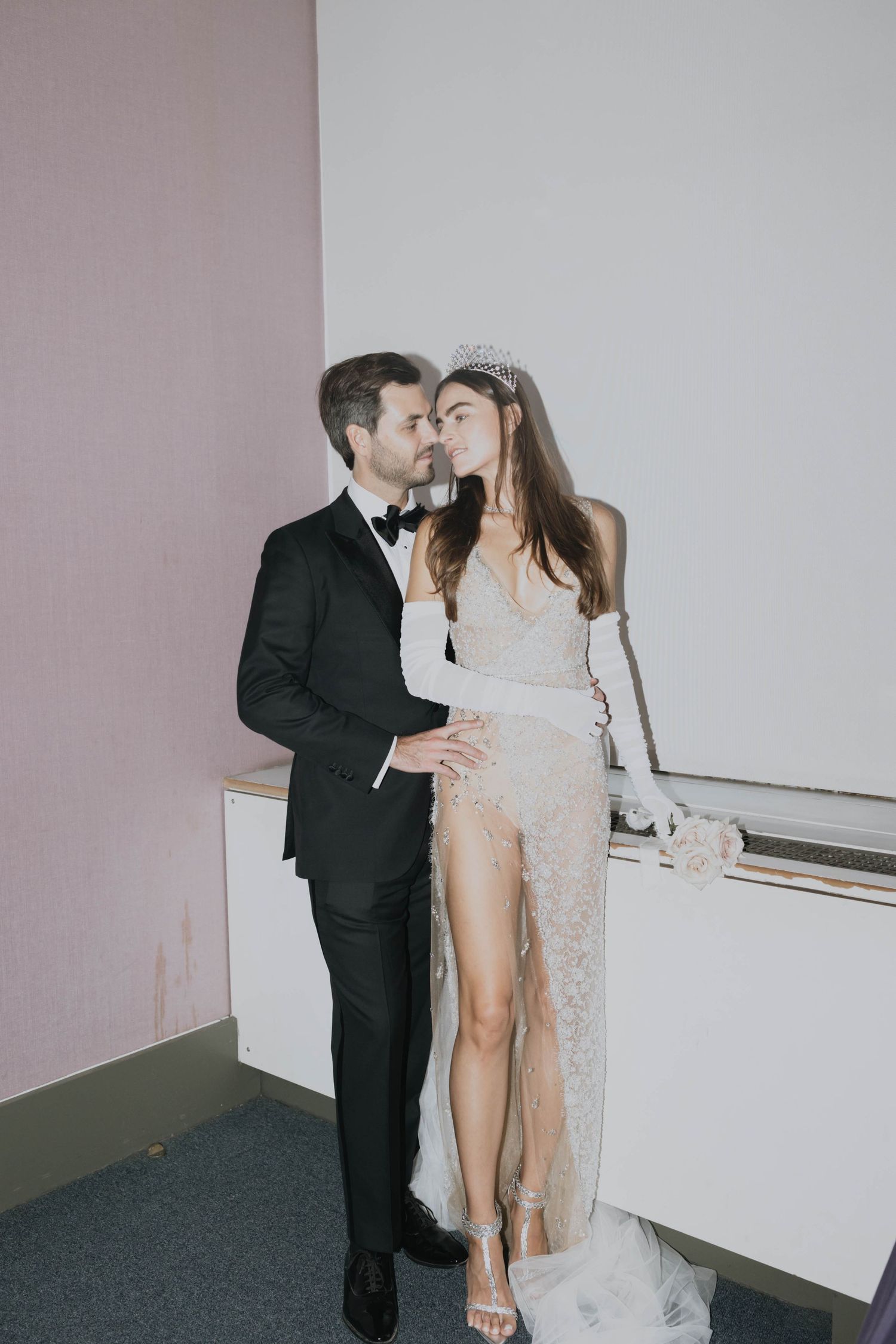 Bride and groom sharing romantic kiss in elegant lace wedding dress with crown and white gloves.