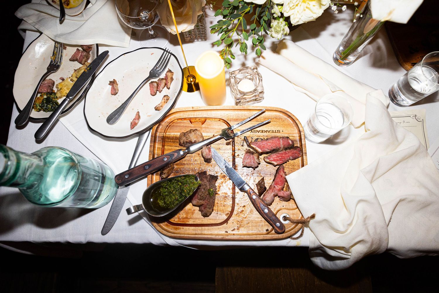 Overhead shot of sliced steak on a wooden board with chimichurri sauce at a wedding dinner.