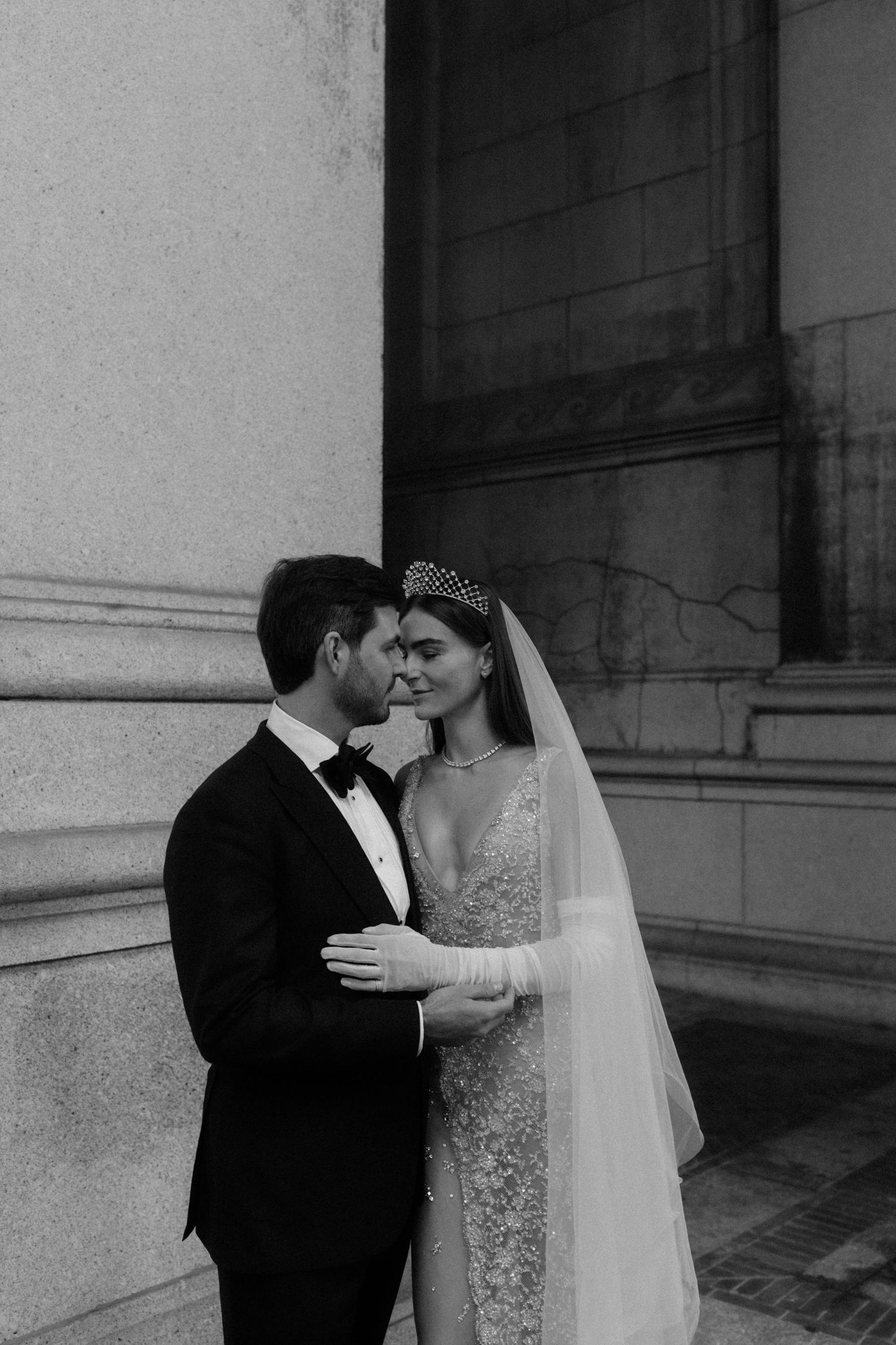 Black and white intimate portrait of bride in crystal crown and groom sharing a tender forehead touch.