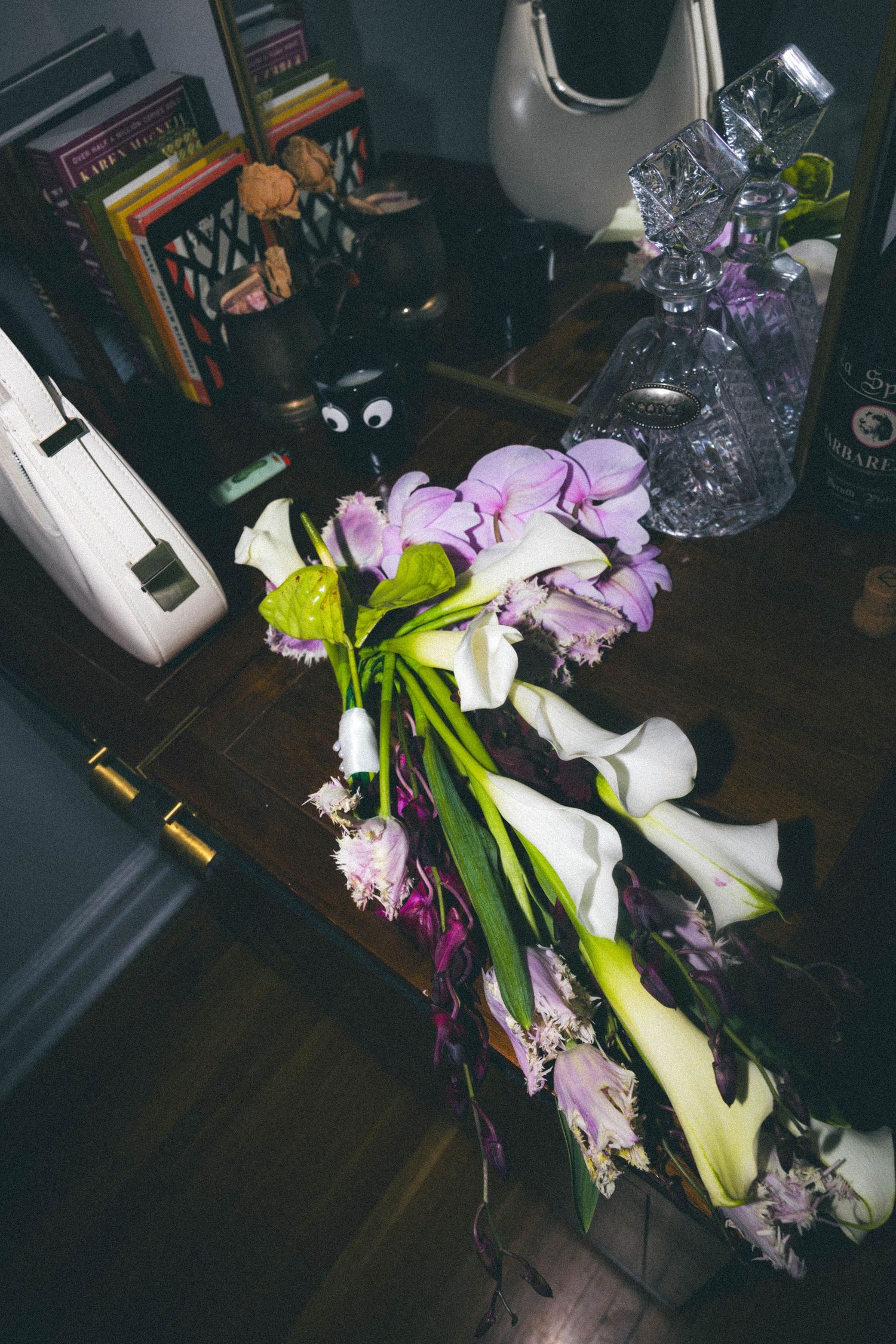 Wedding bouquet of white calla lilies and purple orchids laid on wooden desk with books.