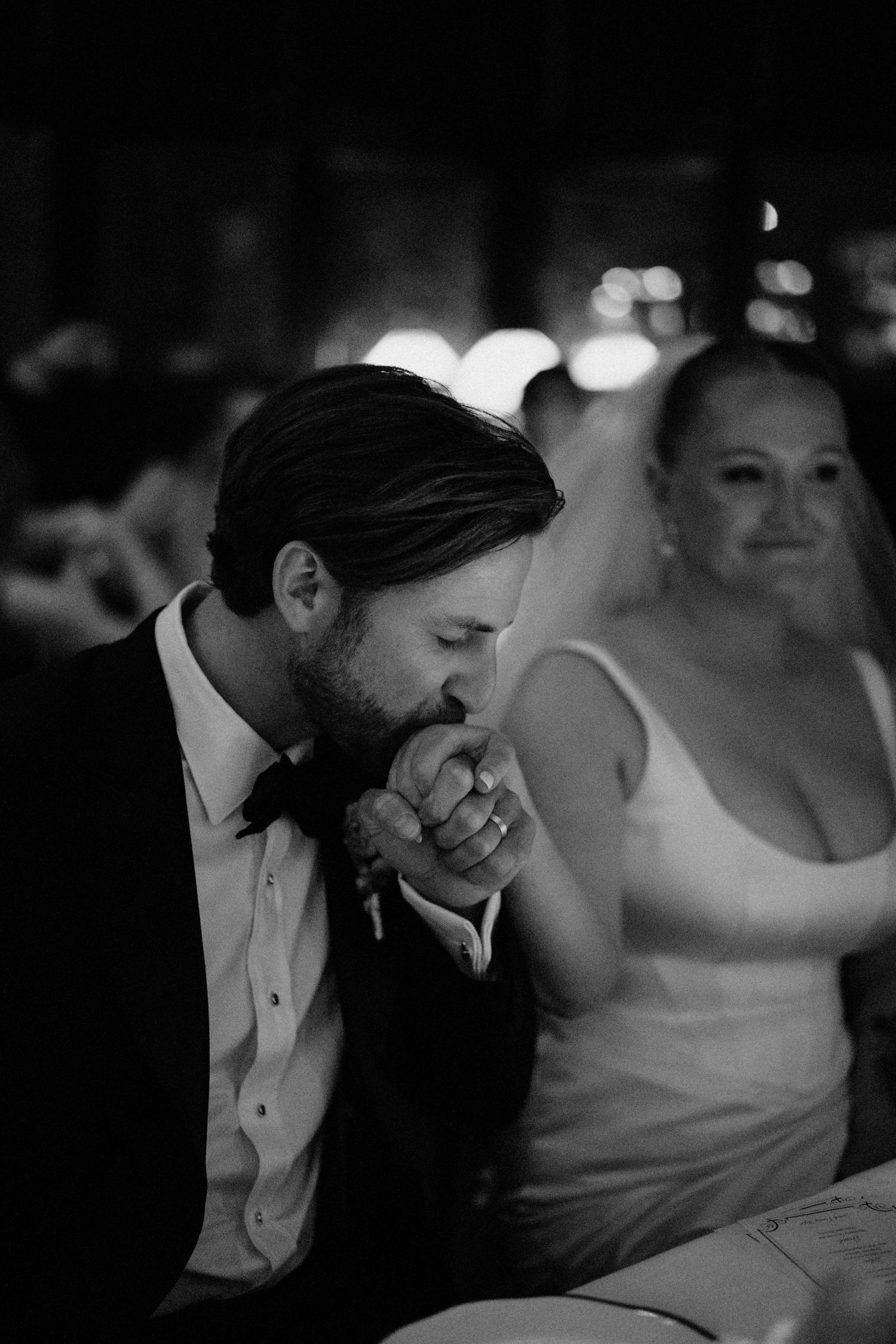Black and white photo of groom kissing bride's hand tenderly at wedding reception.