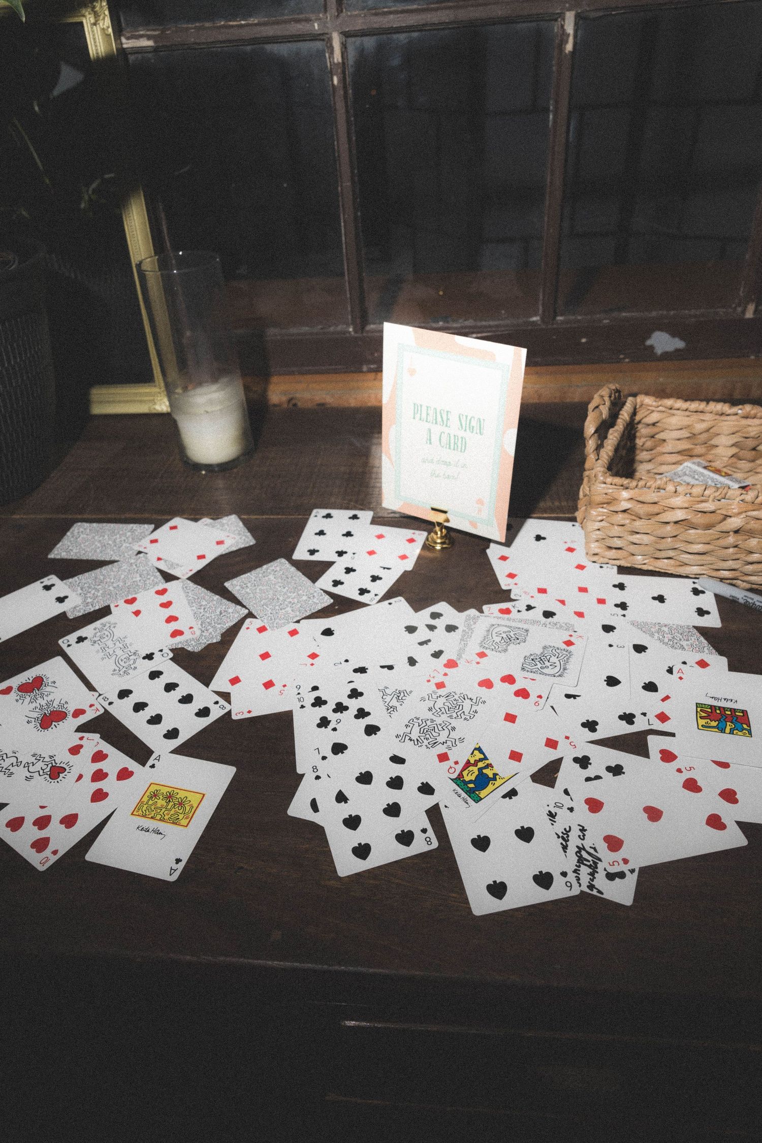 Wedding guest book activity with playing cards spread on a wooden table with a sign saying take a card.