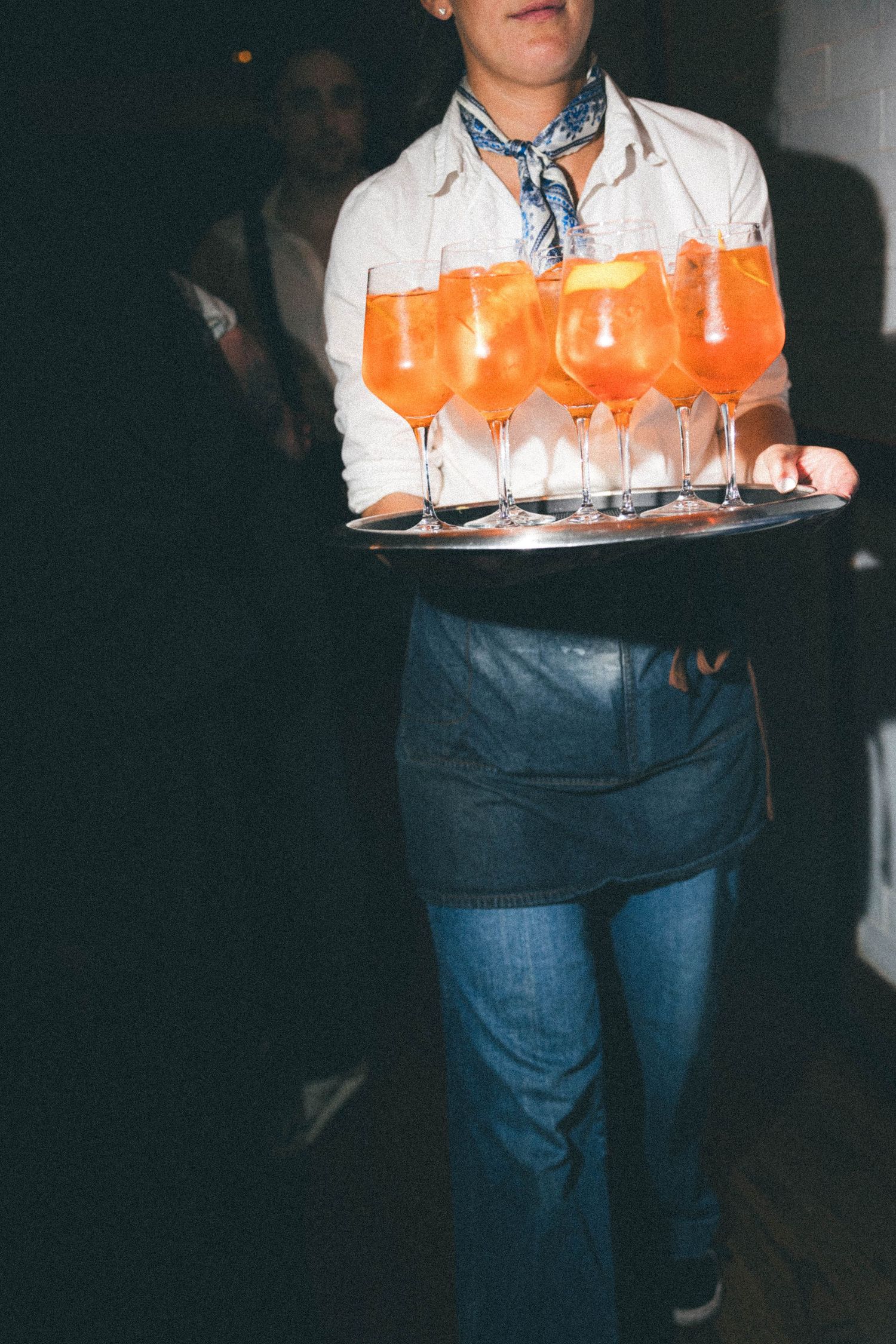 Server carries a tray of orange Aperol Spritz cocktails at an elegant wedding reception event.