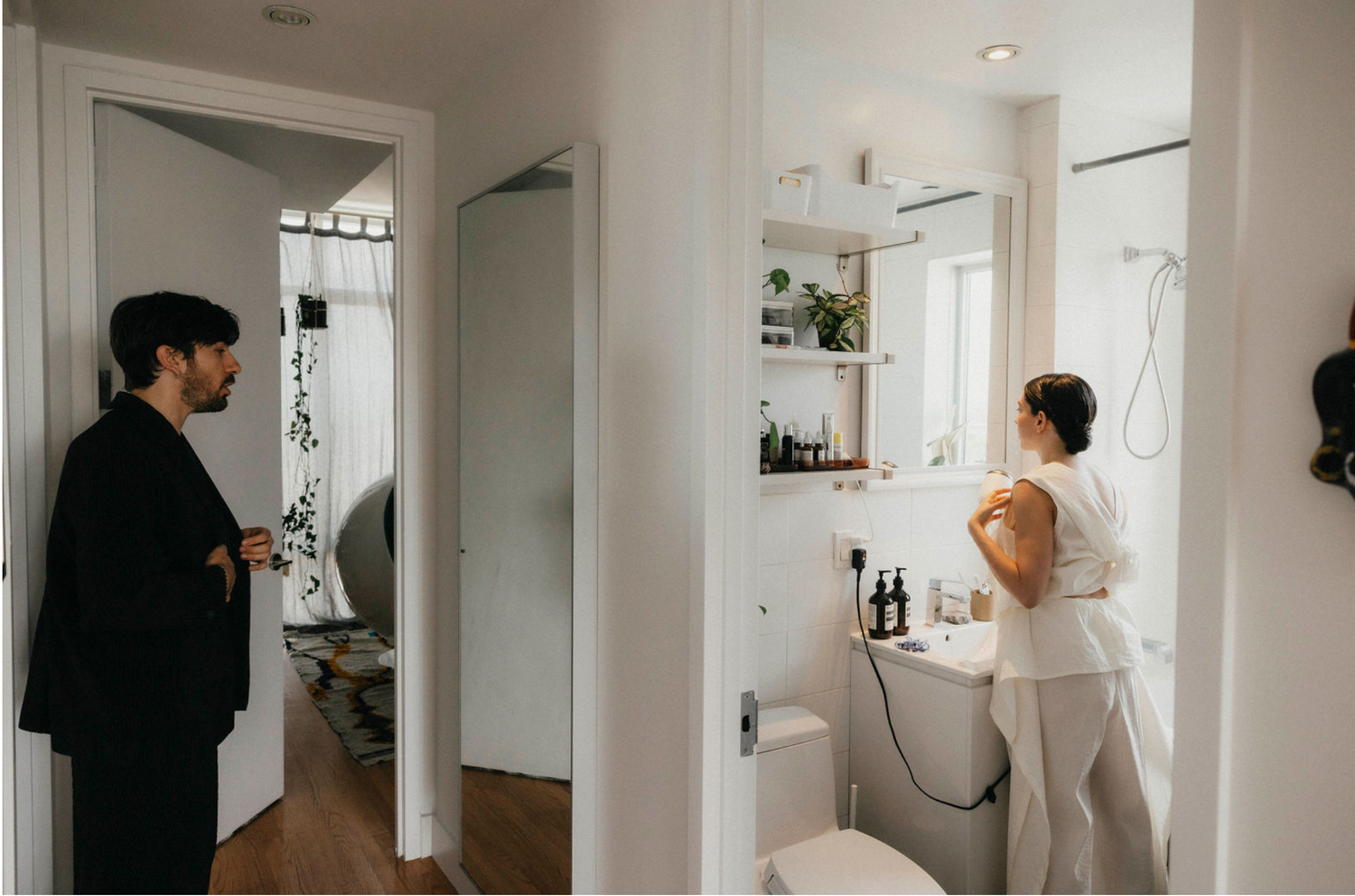 Groom watches bride getting ready in a modern white bathroom before their wedding ceremony.