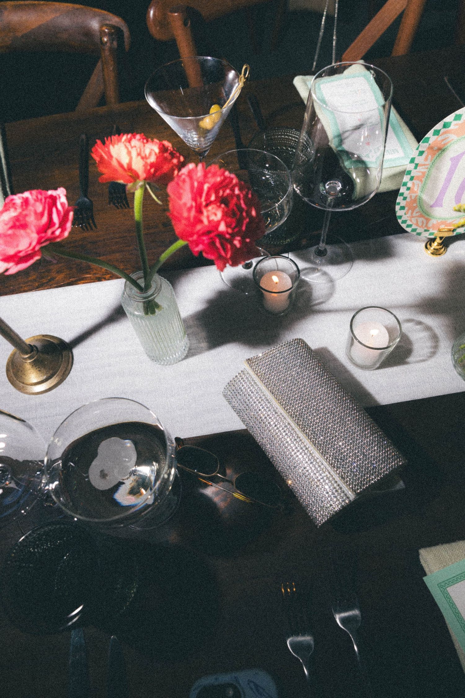 Wedding reception table with red peonies, martini glasses, candles, and a sparkly clutch.