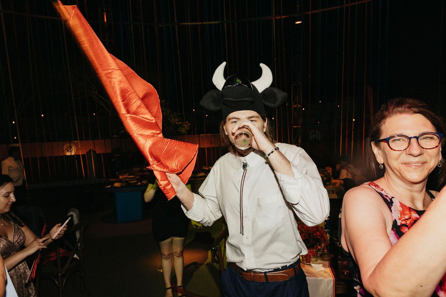 Man wearing bull horns hat waves a red cape at a lively Mexican-themed wedding celebration party.