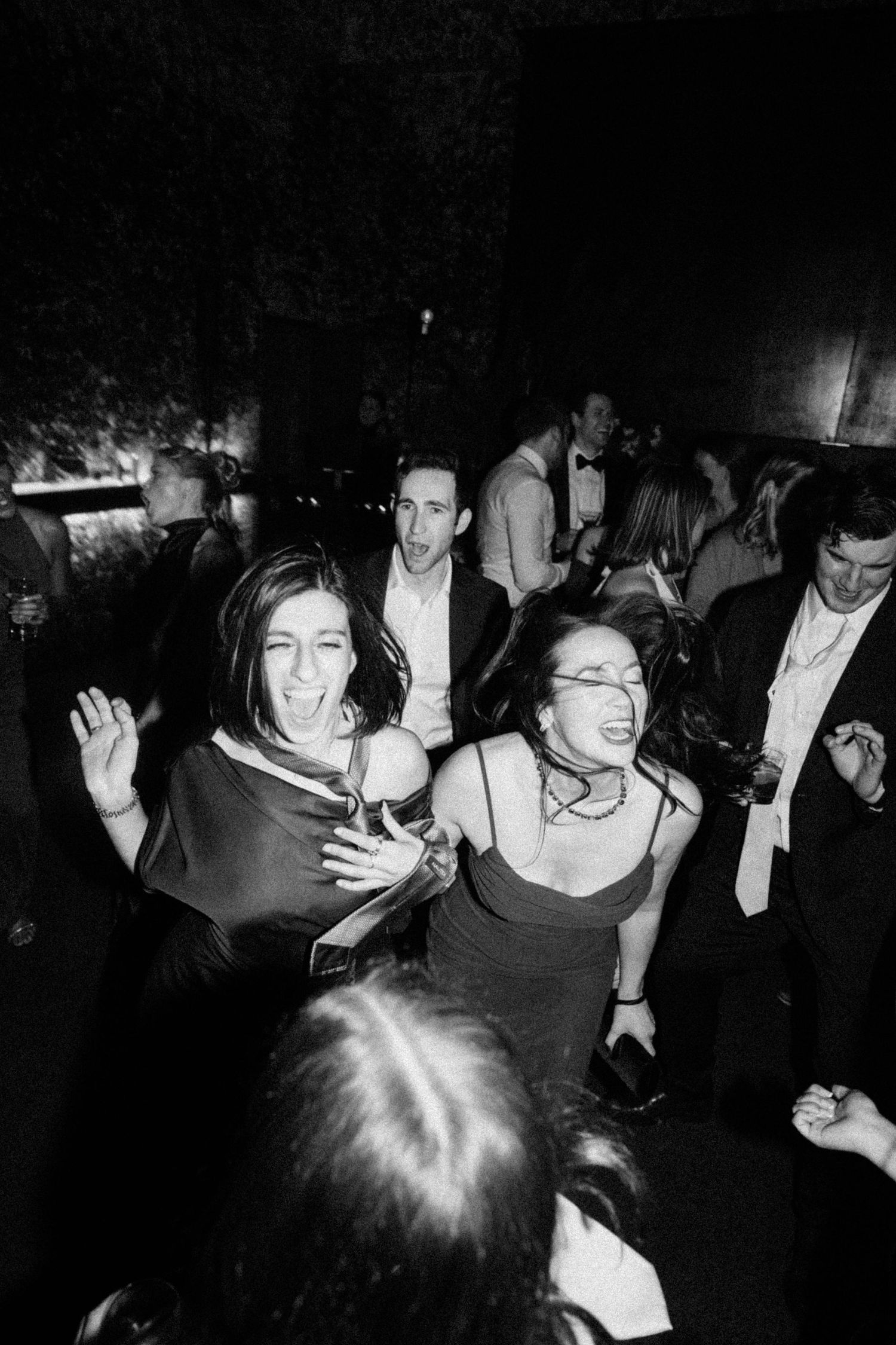 Black and white photo of joyful wedding guests dancing at lively reception party.