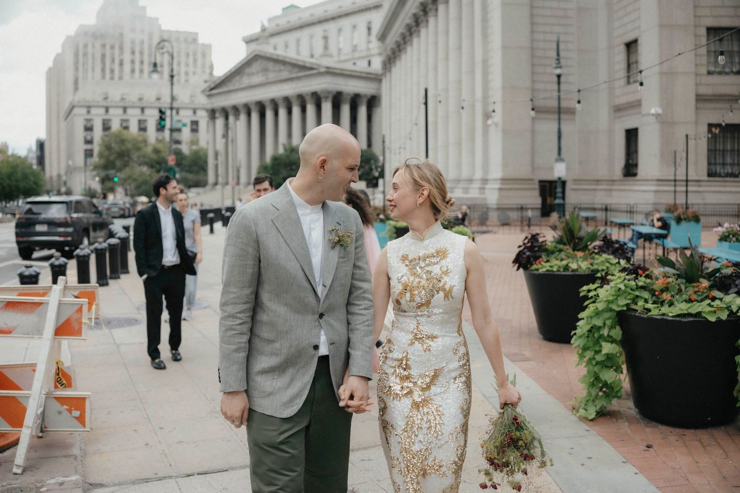 Newlywed couple walks hand in hand outside historic courthouse building on wedding day.