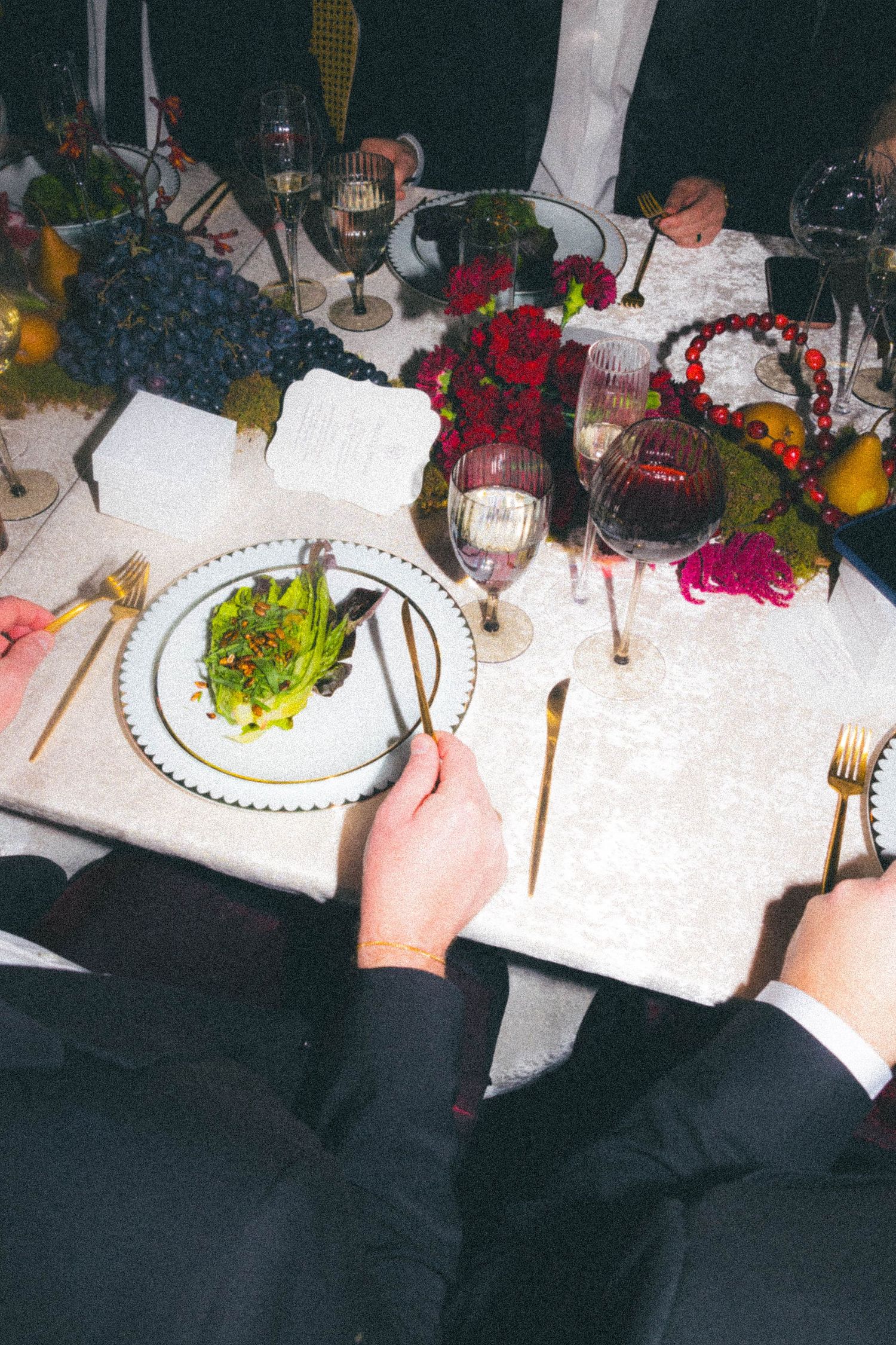 Overhead view of wedding guest eating salad at elegantly set table with gold cutlery and wine.