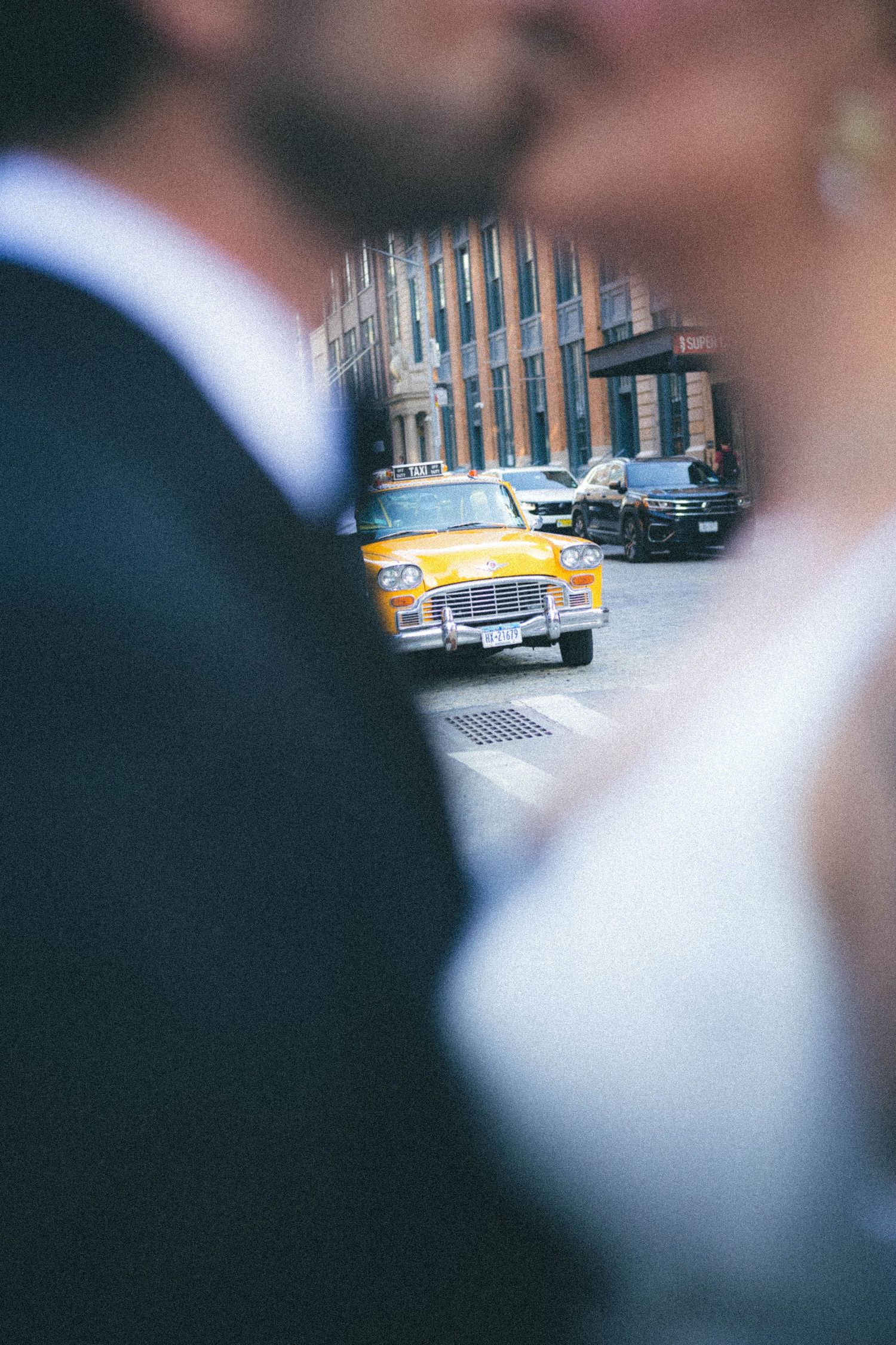 Vintage yellow taxi cab framed between blurred bride and groom on city street.